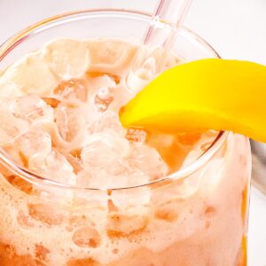 A copycat life's a peach drink with a straw and peach slice in it.