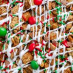 Macro image of Gingerbread Chex Mix showing texture of cereal coated in white chocolate, red and green candies, and sprinkles.