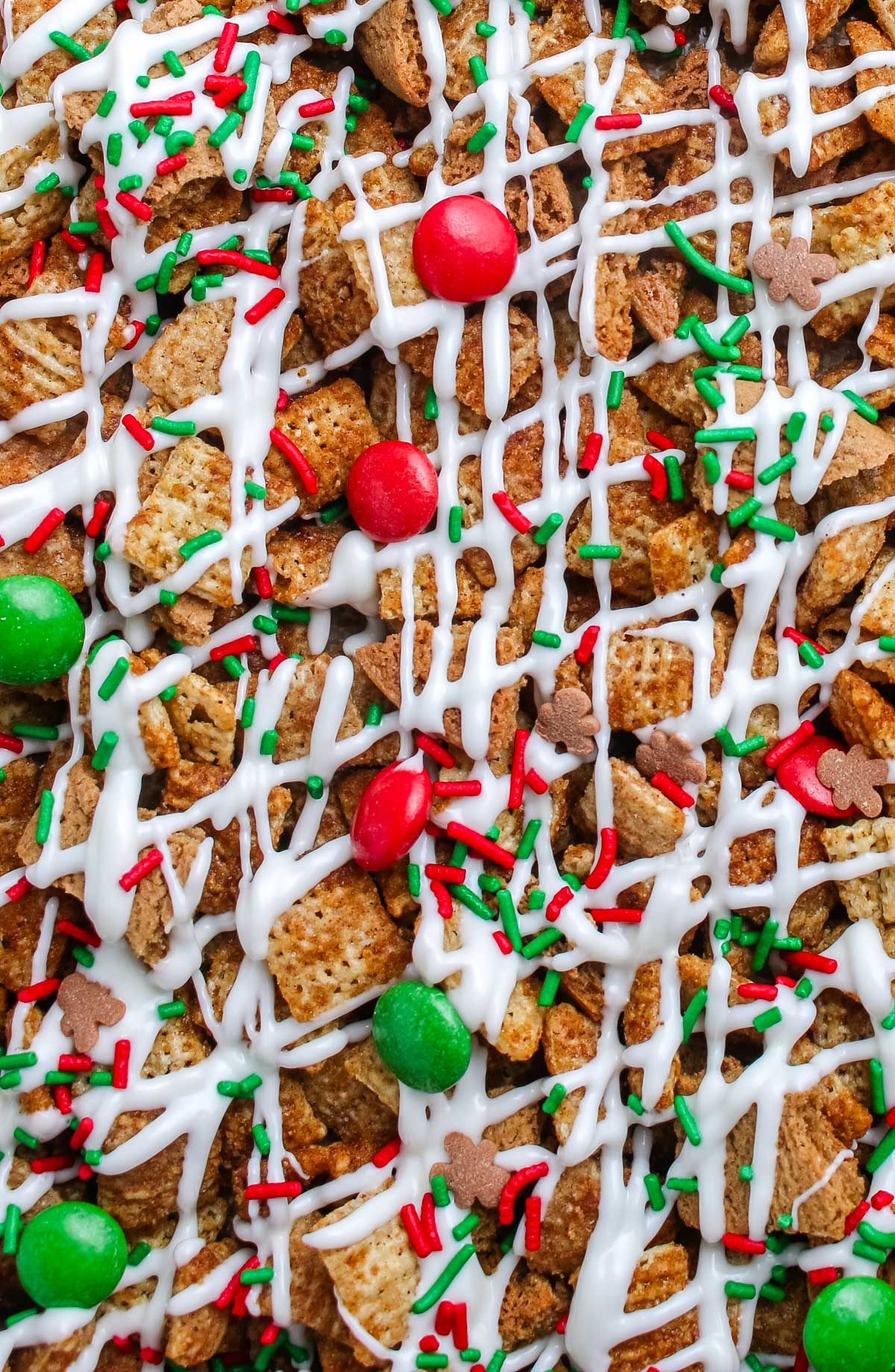 Macro image of Gingerbread Chex Mix showing texture of cereal coated in white chocolate, red and green candies, and sprinkles.