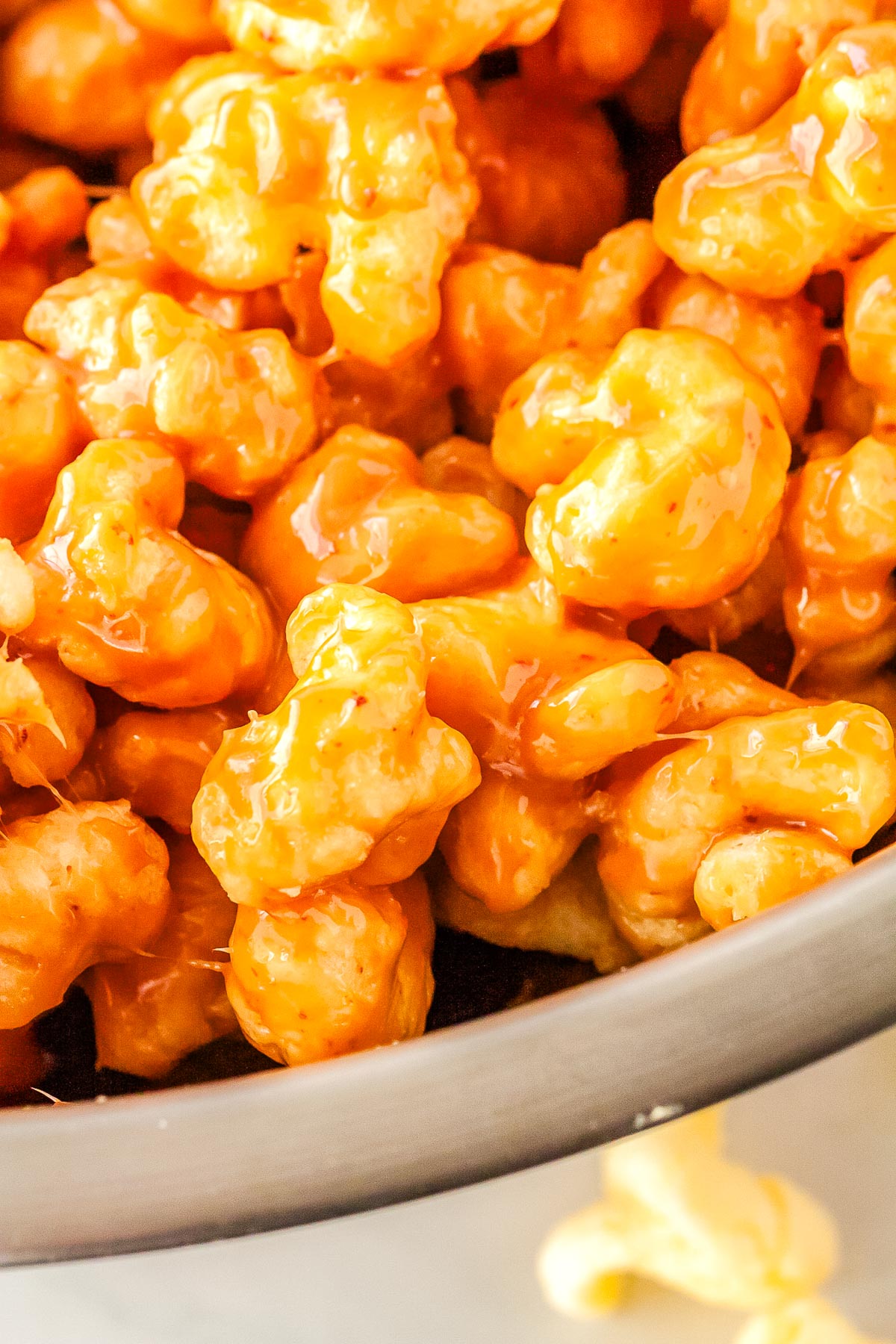 Caramel coated puffed corn pieces glistening with buttery homemade caramel in a close up shot.