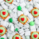 Close up of green puppy chow mixed with green candies and heart topped pretzels spread across a surface.