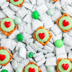 Close up of green puppy chow mixed with green candies and heart topped pretzels spread across a surface.