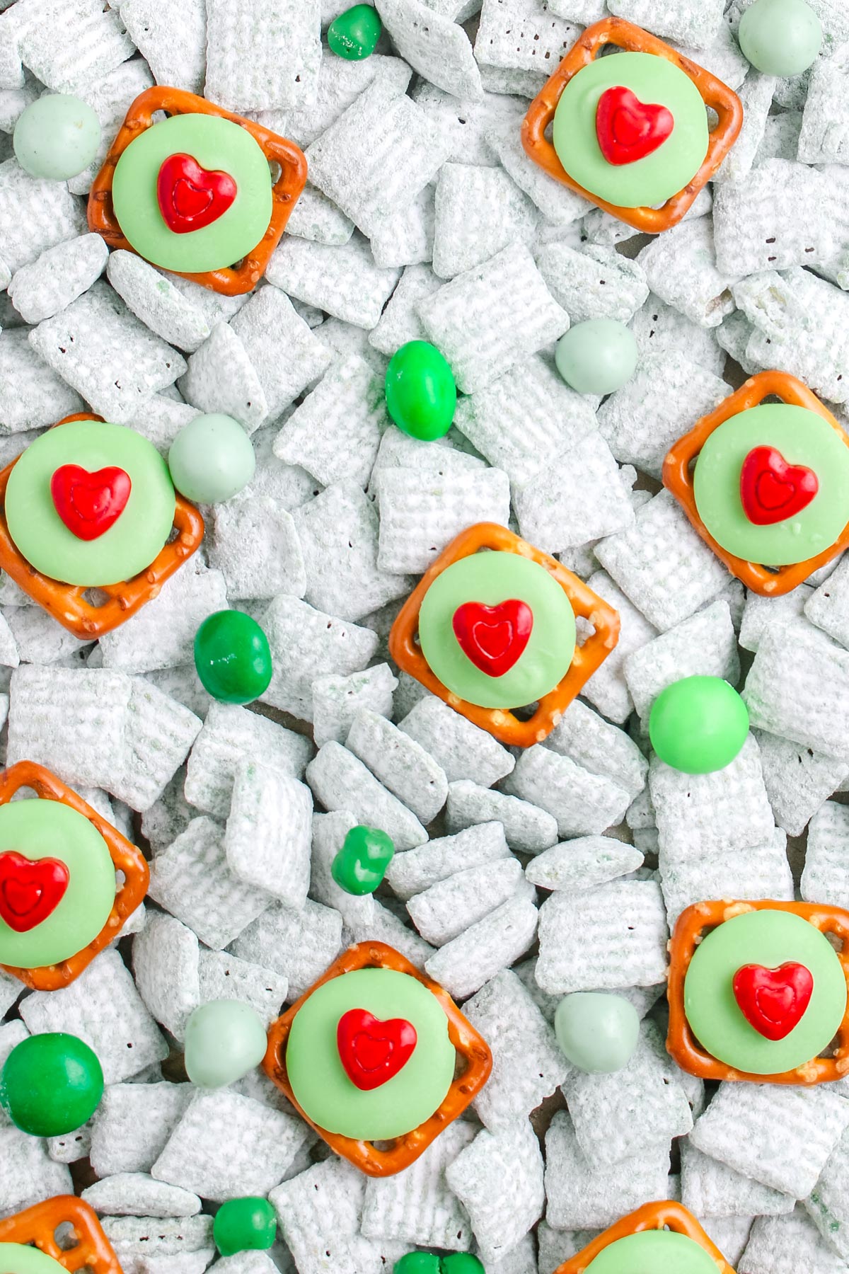 Close up of green puppy chow mixed with green candies and heart topped pretzels spread across a surface.