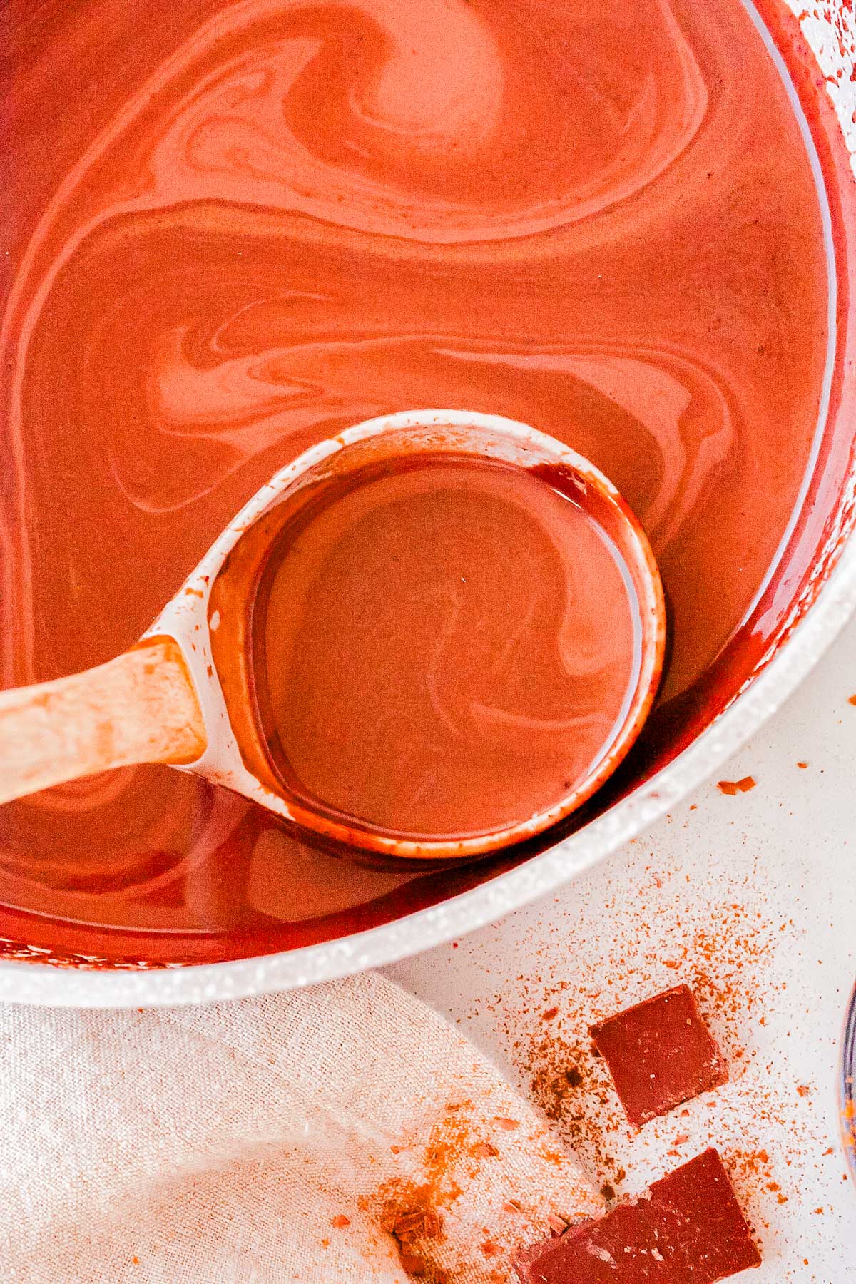 Wooden ladle scooping creamy Cinnamon Hot Chocolate from a pot with swirls of melted chocolate on the surface.