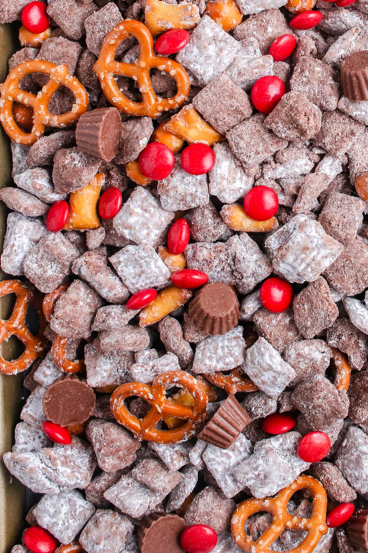 Close up of Reindeer Chex Mix on a sheet pan showing coated cereal, pretzels, red candies, and peanut butter cups.