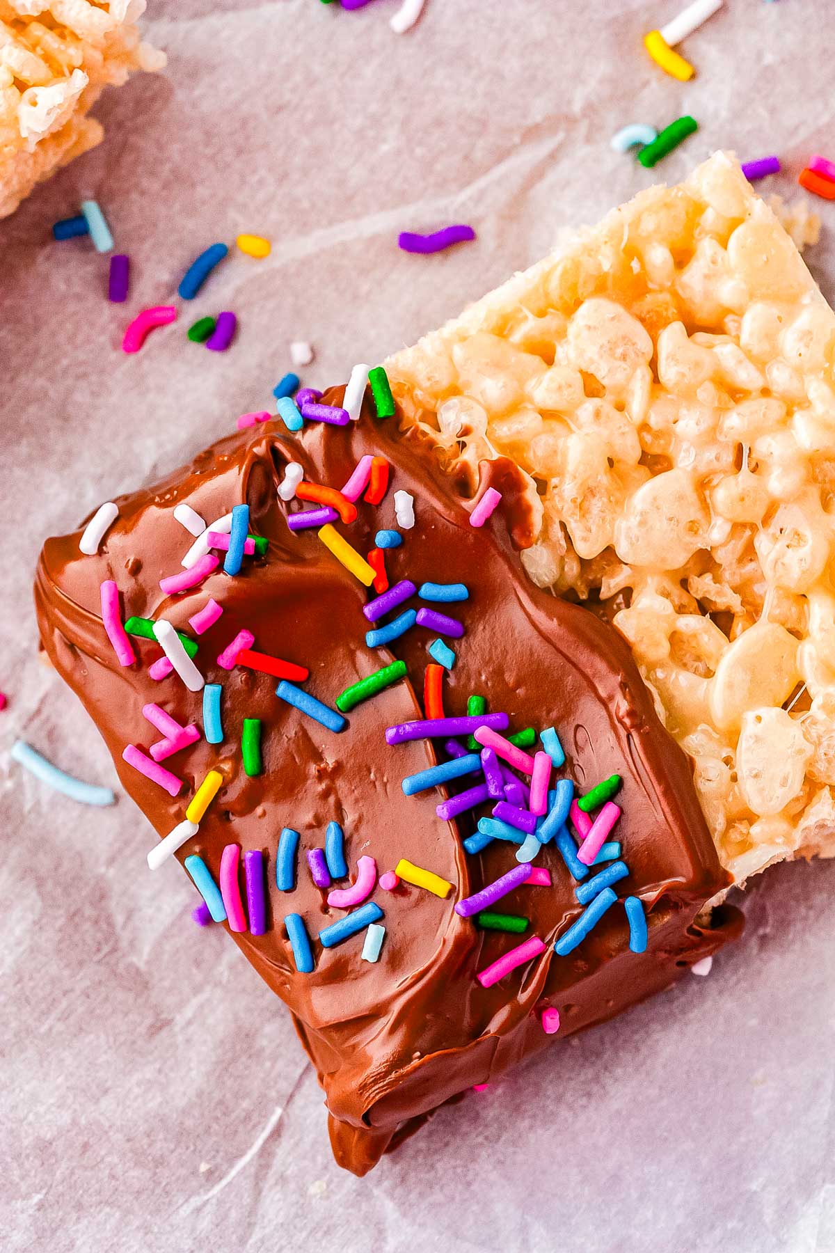 Chocolate dipped Rice Crispy treats with colorful sprinkles on parchment paper.