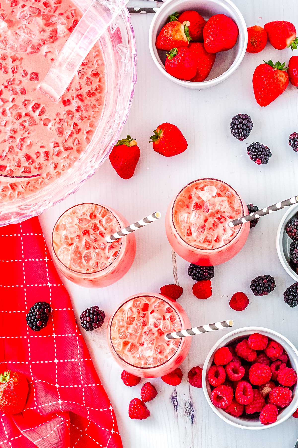 Overhead view of Polar Punch in a glass punch bowl surrounded by berry filled glasses, fresh strawberries, raspberries, and blackberries.