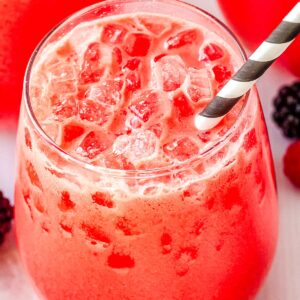 Close up shot of a glass filled with creamy berry Polar Punch and crushed ice with a black and white striped straw.