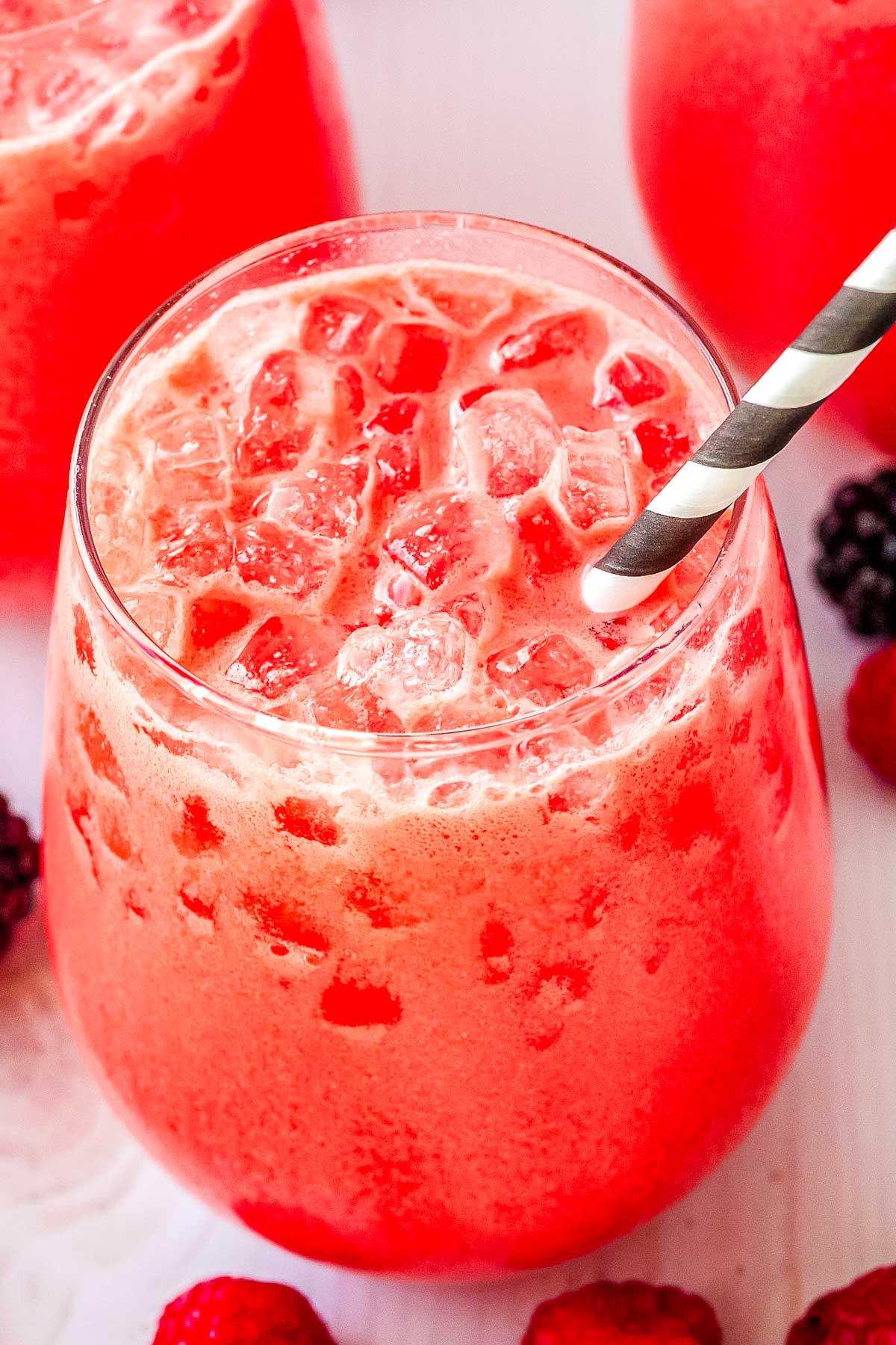 Close up shot of a glass filled with creamy berry Polar Punch and crushed ice with a black and white striped straw.