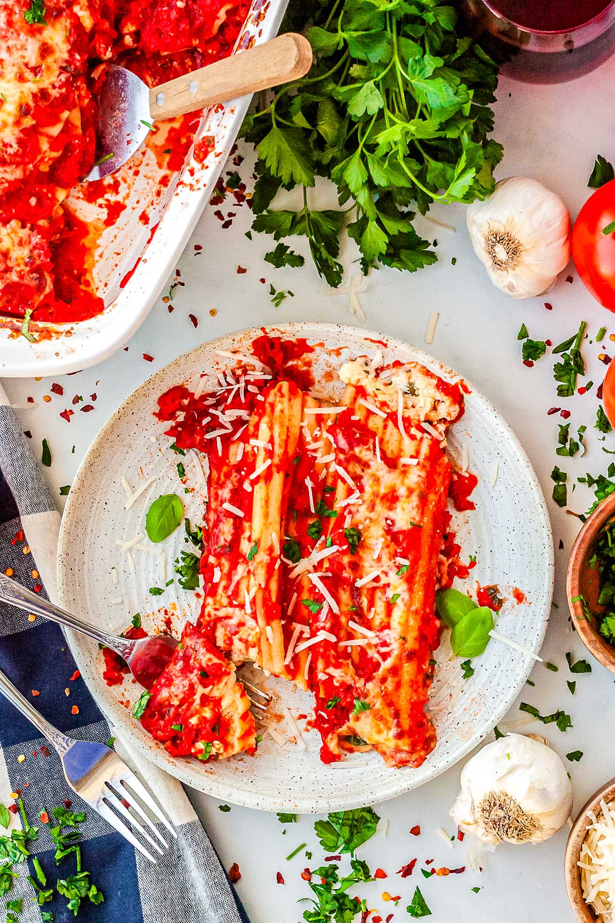 A plated serving of two manicotti rolls covered in red sauce and cheese, cut open with a fork to show the white ricotta filling inside.