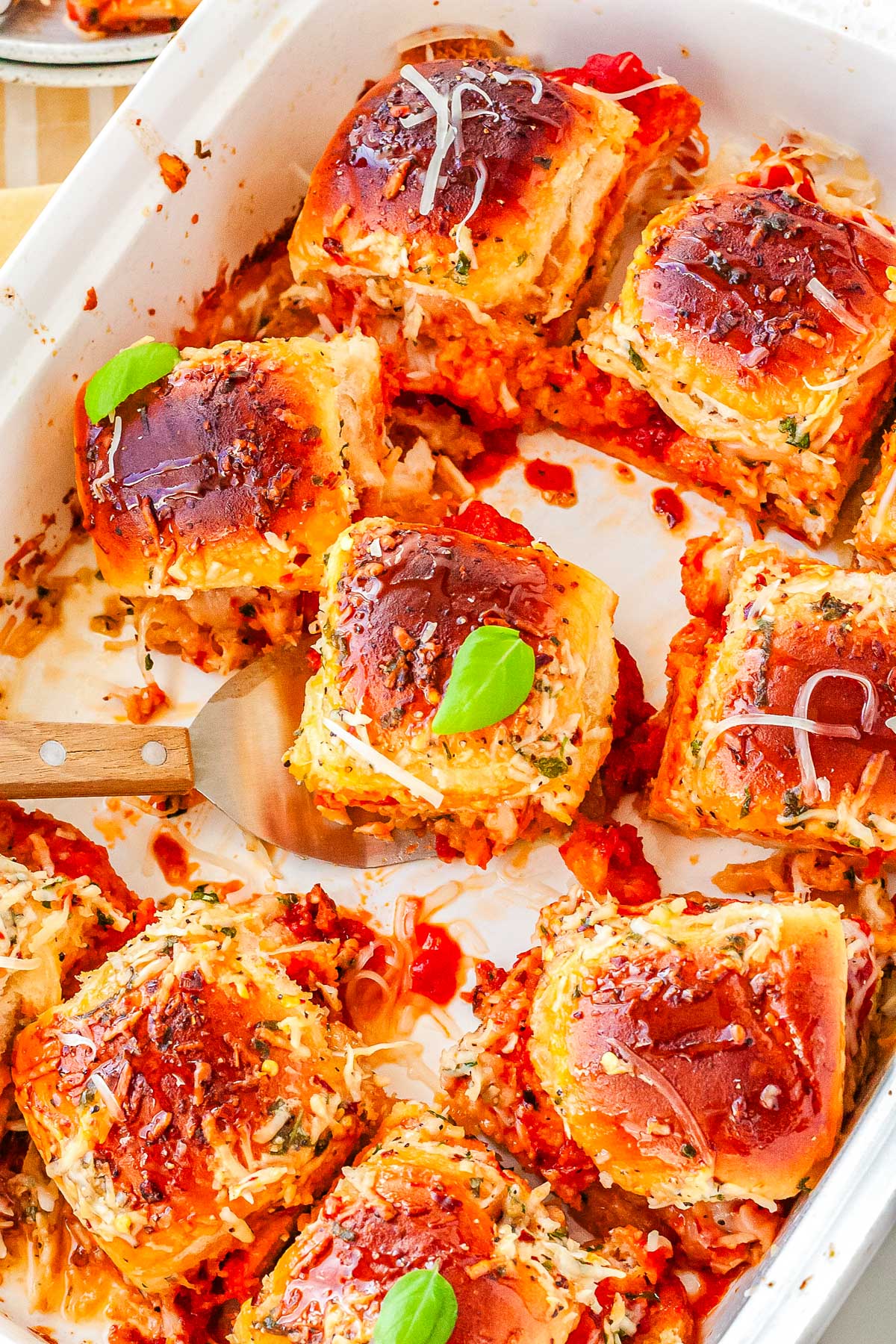 An overhead view of a baking dish filled with pull-apart chicken sliders, with several pieces removed to show the saucy, cheesy interior.