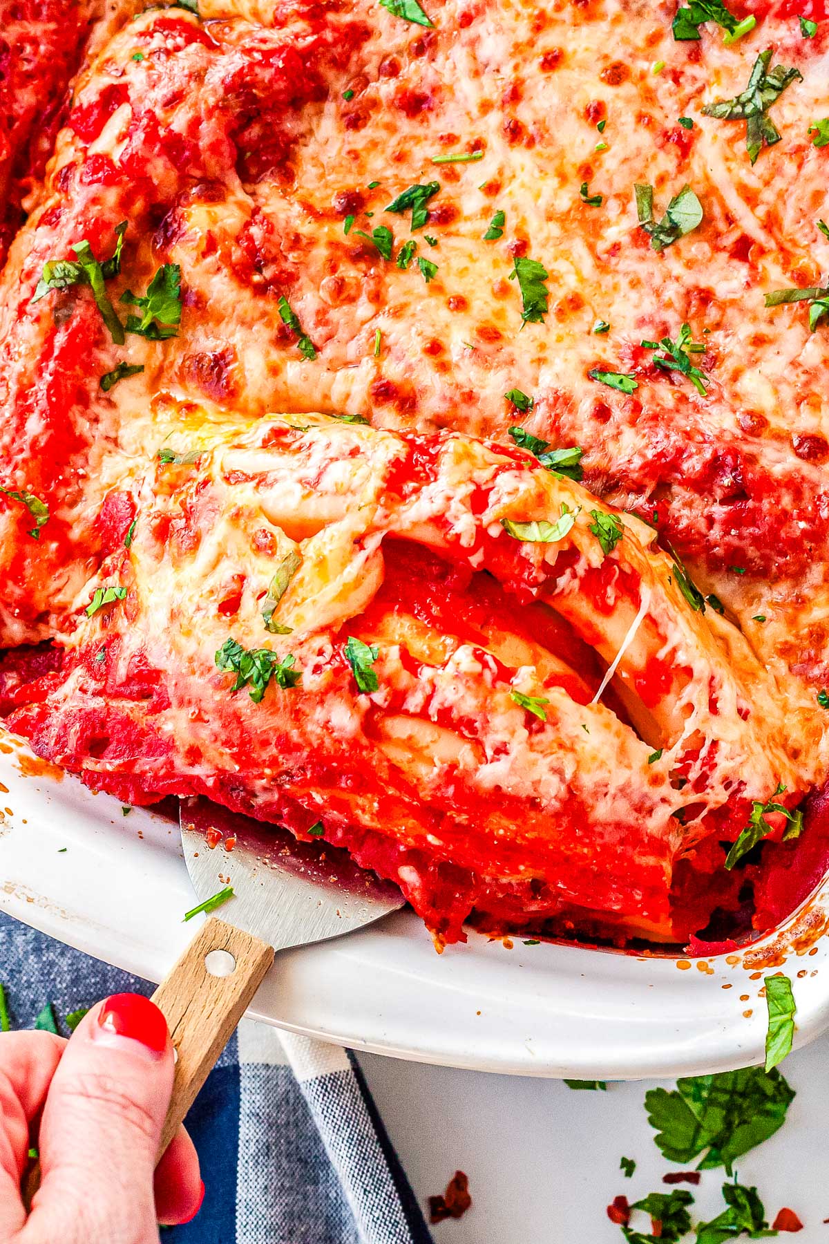 A close-up shot of a spatula lifting a cheesy manicotti roll out of the baking dish, revealing the saucy layers and creamy interior.