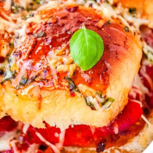 A macro shot of a golden brown slider bun topped with a glossy hot honey glaze, crushed red pepper flakes, and a fresh basil leaf.