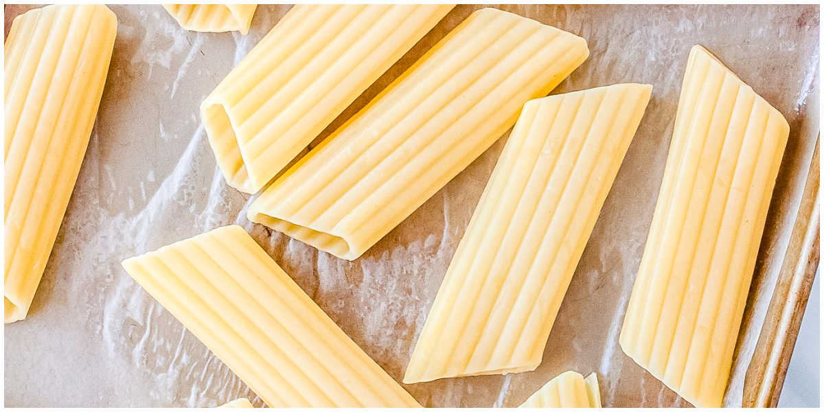 Cooked and drained manicotti pasta shells arranged on a baking sheet to cool slightly before filling.