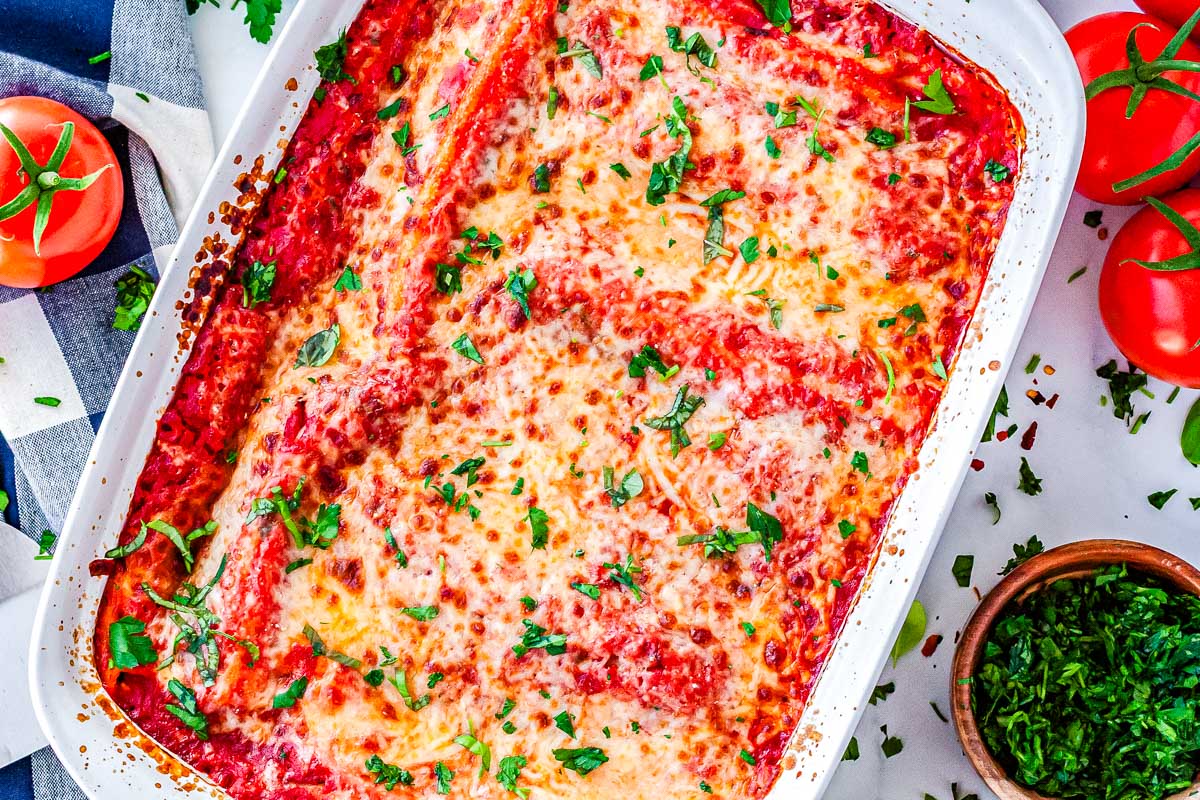 An overhead view of the full baked casserole dish, featuring golden melted cheese, rich tomato sauce, and a garnish of fresh chopped basil.