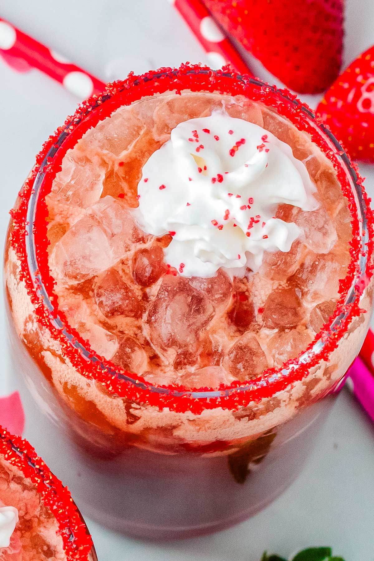 Strawberry dirty Dr Pepper drink with pebble ice and whipped cream, garnished with red sugar rim and surrounded by fresh strawberries.