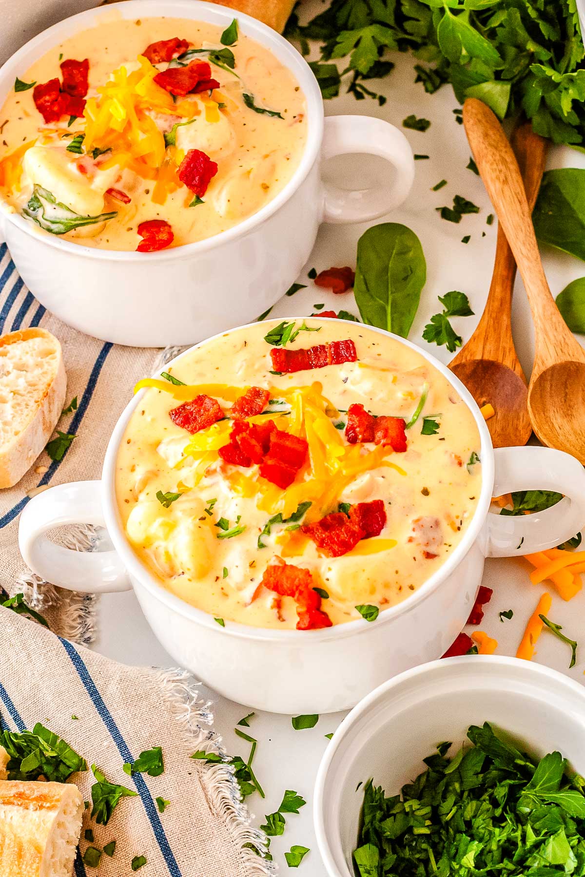 An overhead view of a white bowl filled with creamy orange cheddar gnocchi soup, topped with crispy bacon bits, fresh parsley, and extra cheese.