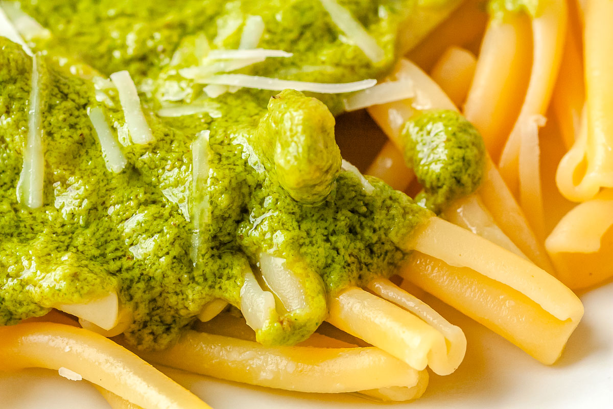 A close-up shot of hot pasta coated in green lemon pesto sauce and sprinkled with freshly grated Parmesan cheese.