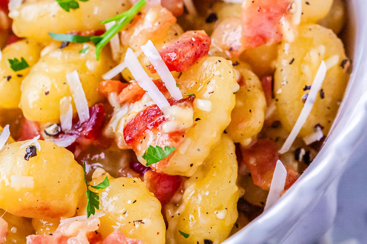 Close up of crispy gnocchi carbonara with pancetta, melted Pecorino Romano, cracked black pepper, and fresh parsley.