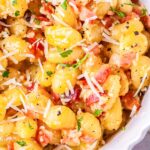 Close up detail of roasted gnocchi carbonara with crispy pancetta and melted cheese coating each piece.