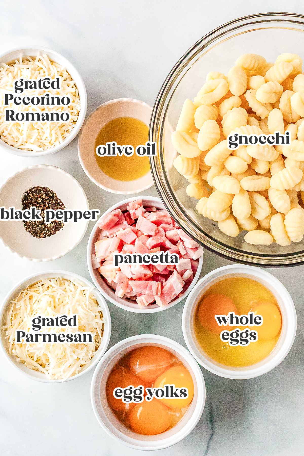 Overhead ingredients shot for sheet pan gnocchi carbonara including gnocchi, pancetta, eggs, Pecorino Romano, Parmesan, olive oil, and black pepper.