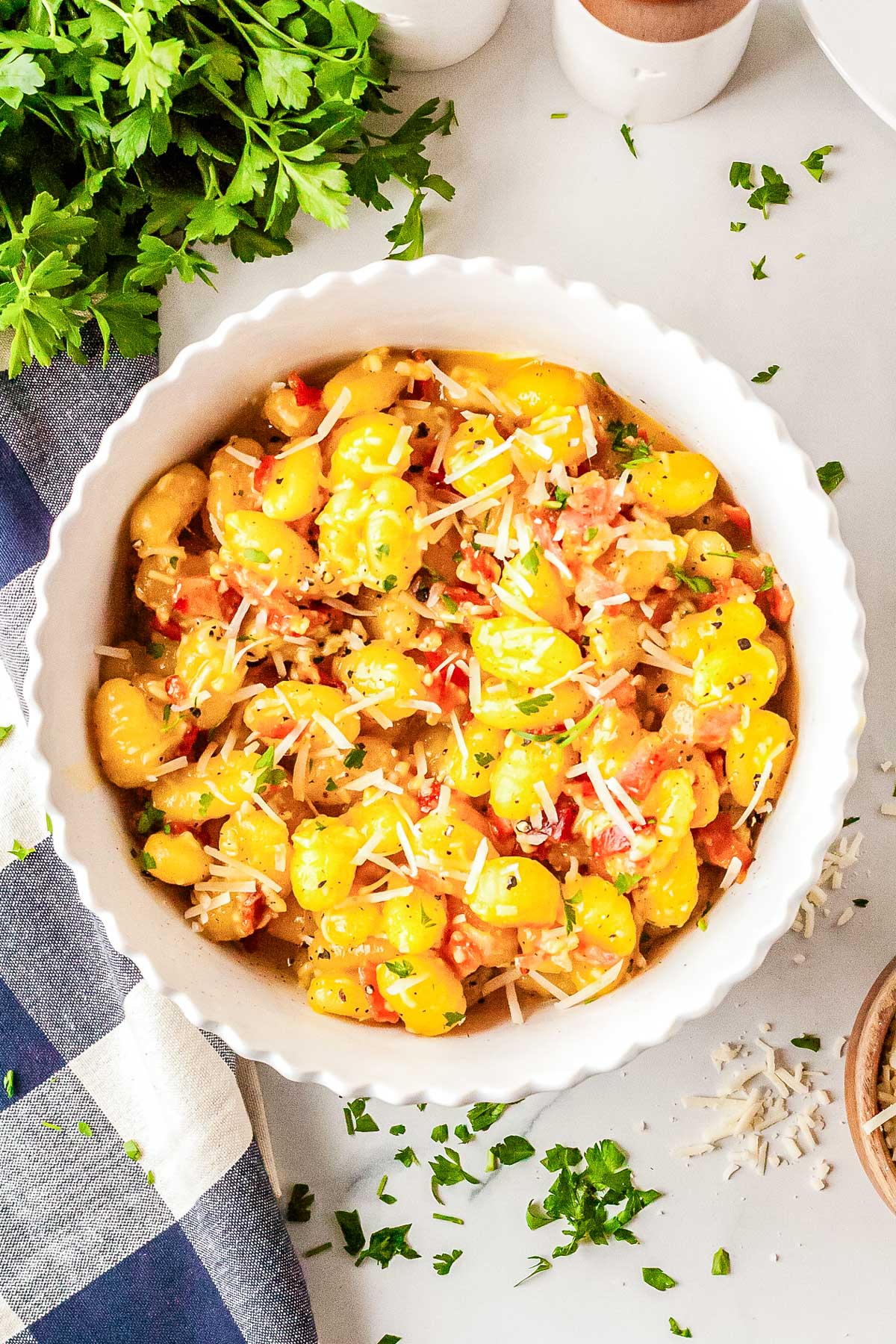 Overhead view of sheet pan gnocchi carbonara in a white dish garnished with grated cheese and parsley.