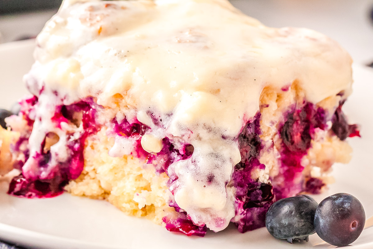 Blueberry swim biscuit topped with cream cheese icing showing juicy baked blueberries and soft biscuit texture.