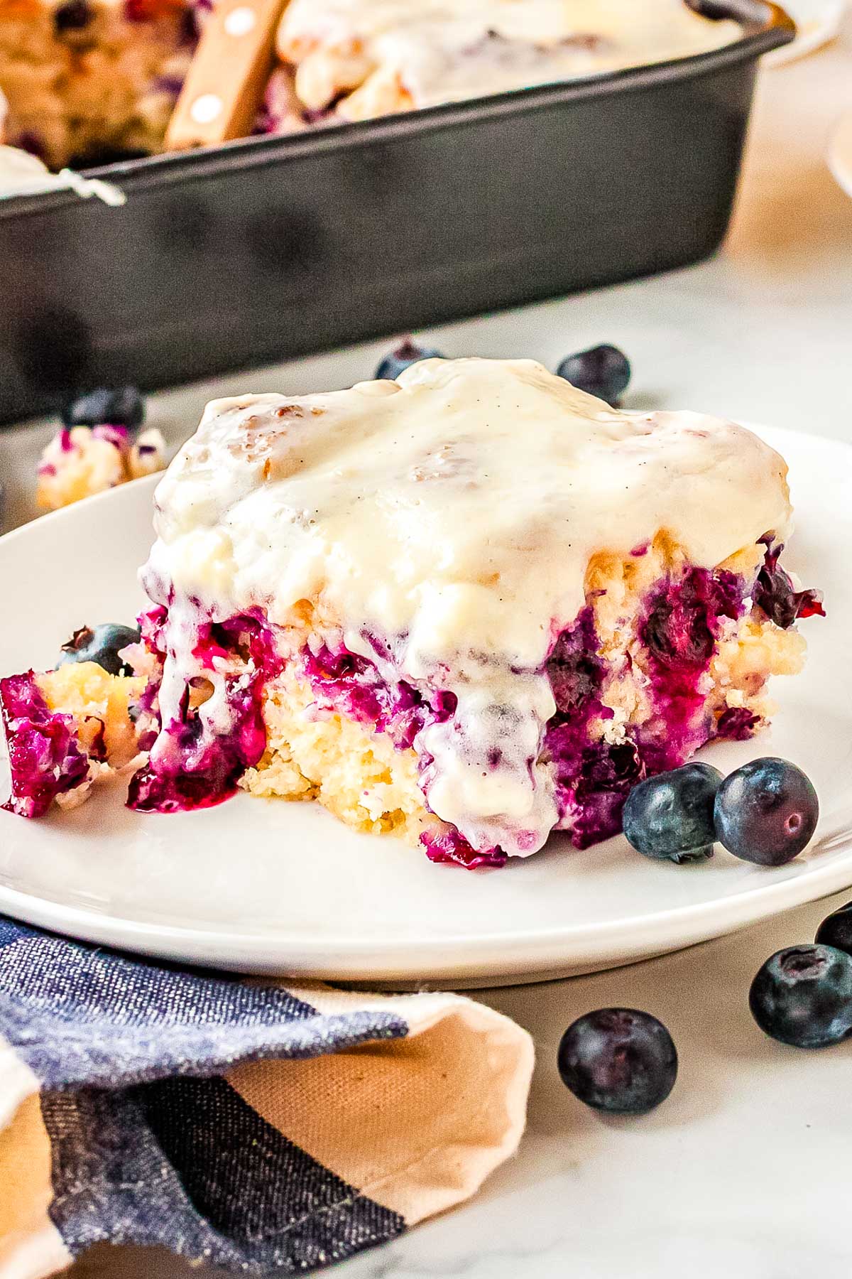 Blueberry swim biscuit with cream cheese icing served on a plate with fresh blueberries.
