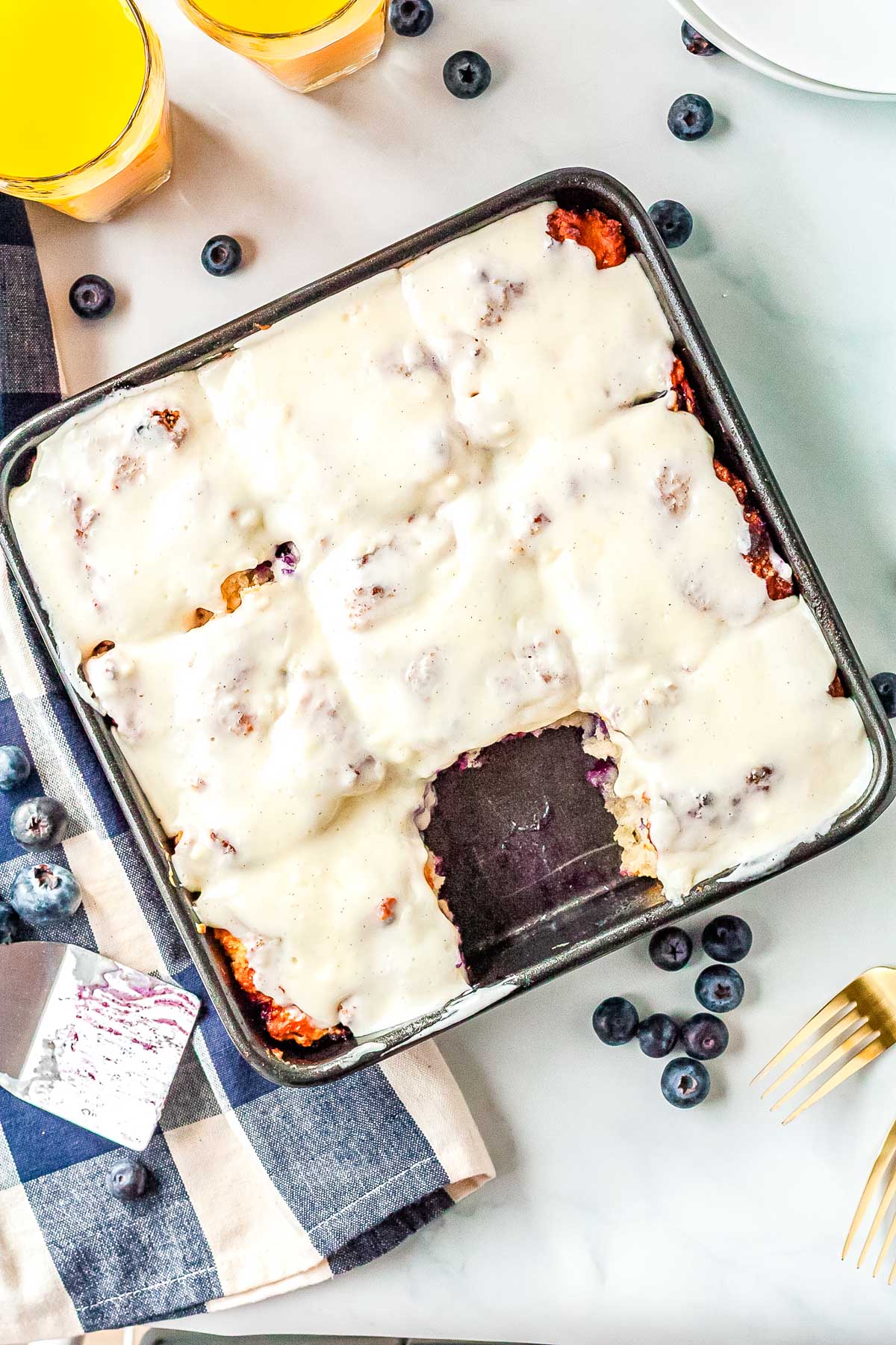Pan of blueberry swim biscuits covered with cream cheese icing with one square removed.