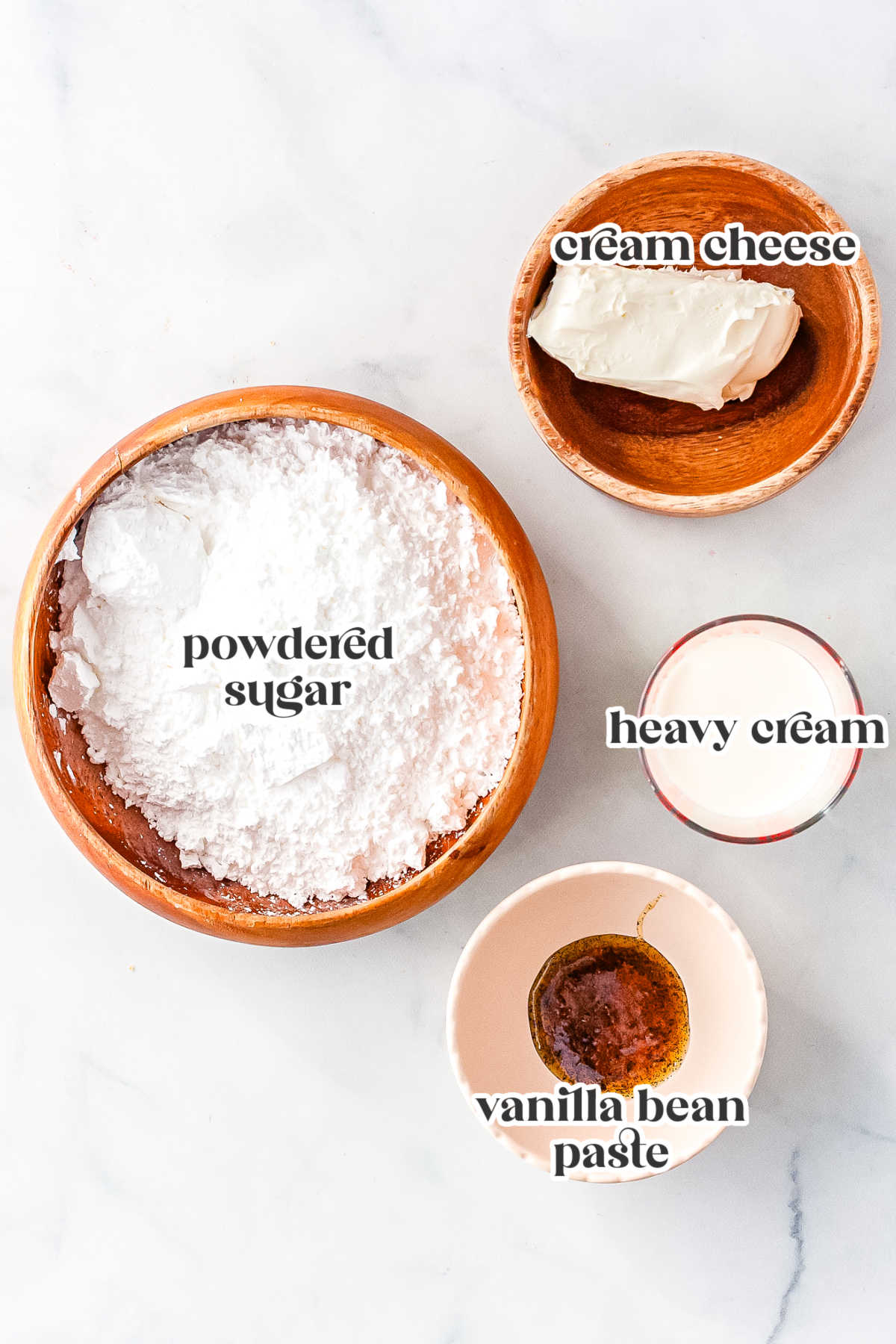 Ingredients for cream cheese icing including powdered sugar, cream cheese, heavy cream, and vanilla bean paste.