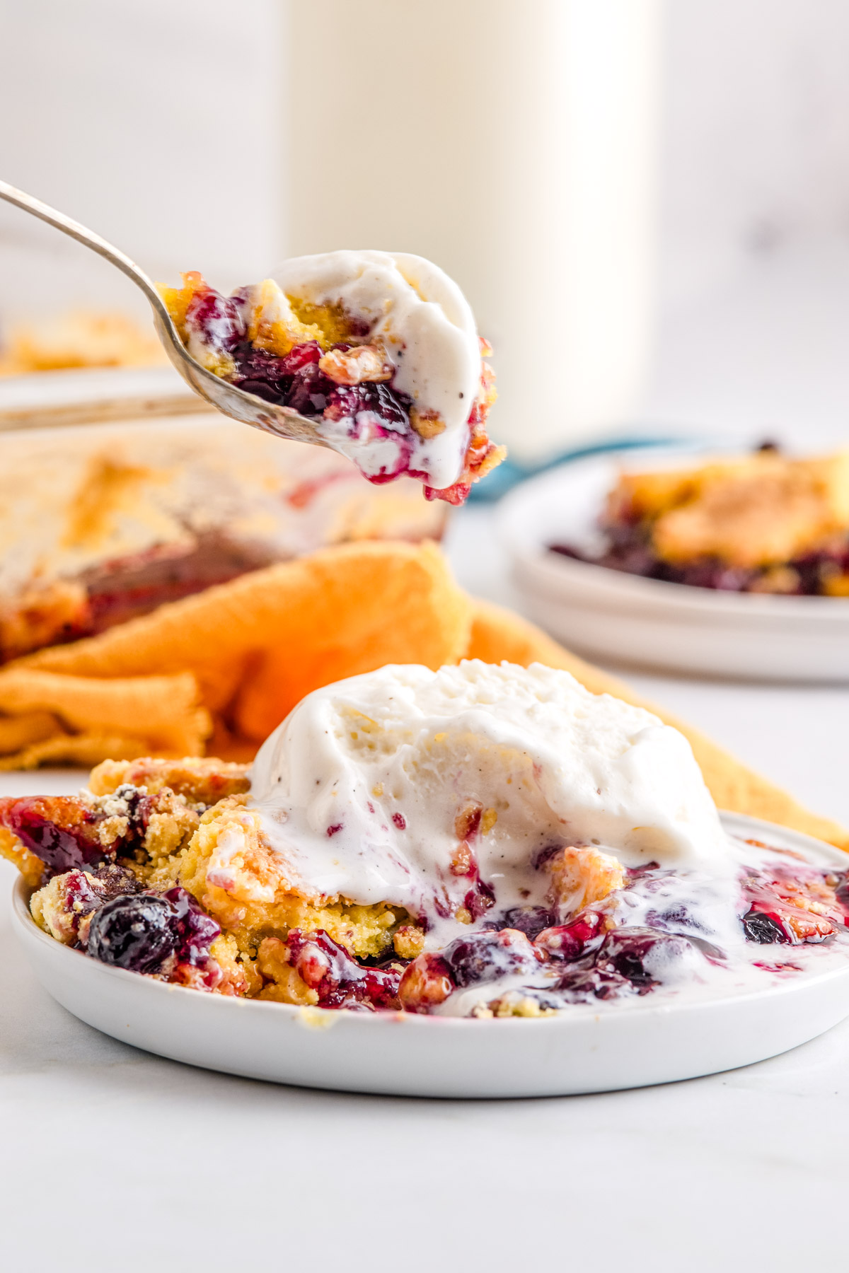 Close-up of blueberry lemon dump cake with vanilla ice cream melting over a spoonful showing creamy and fruit-filled texture.