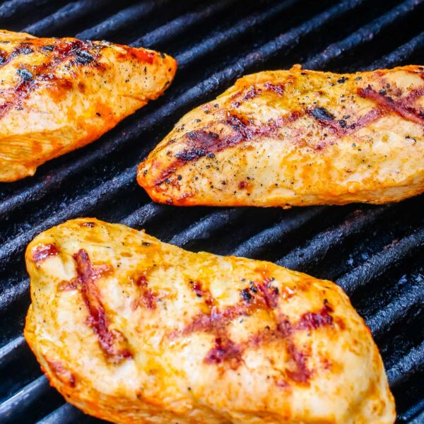 Buffalo chicken breasts cooking on outdoor grill grates with visible char marks.