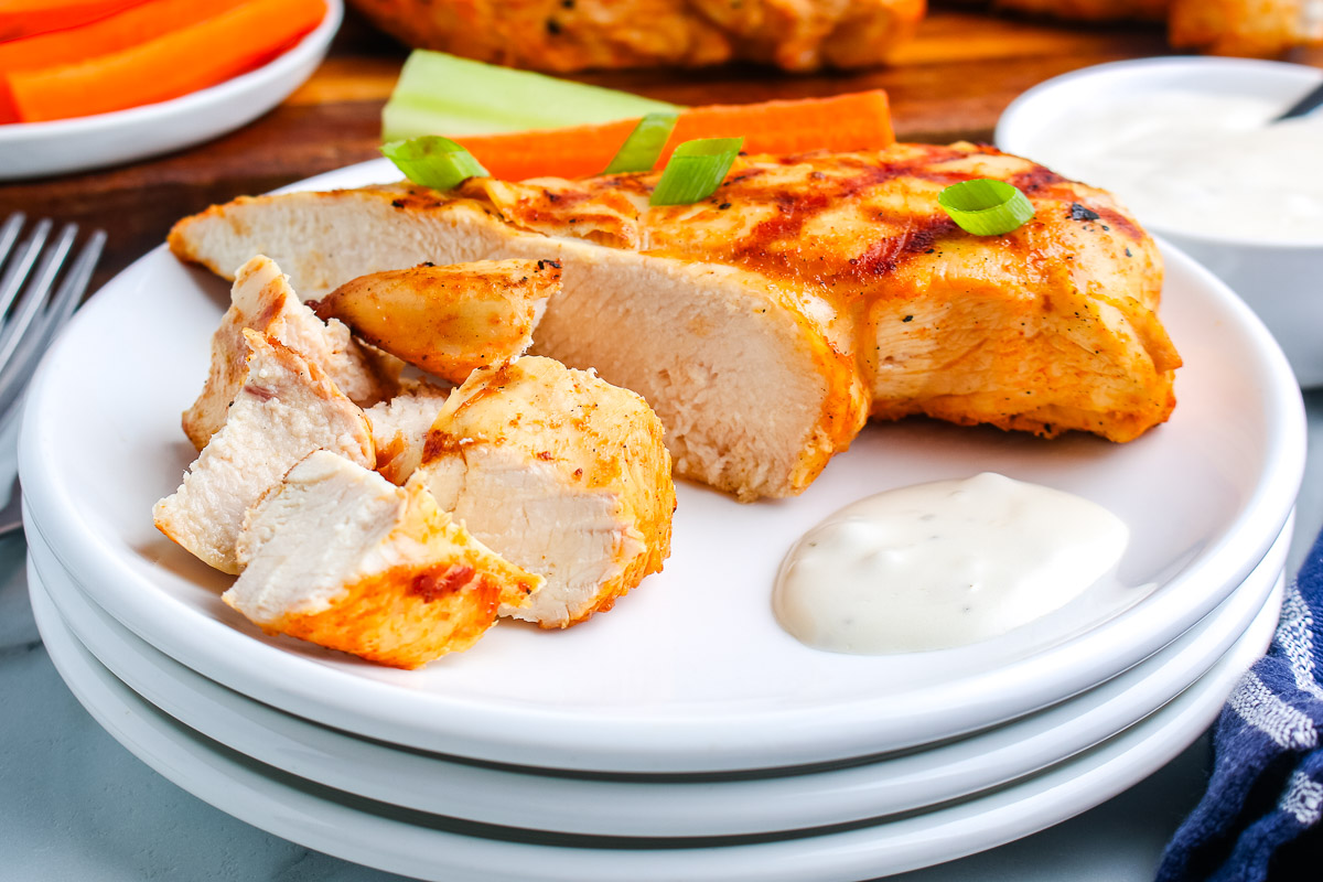 Sliced grilled buffalo chicken breast served with ranch dressing and green onions on a white plate.
