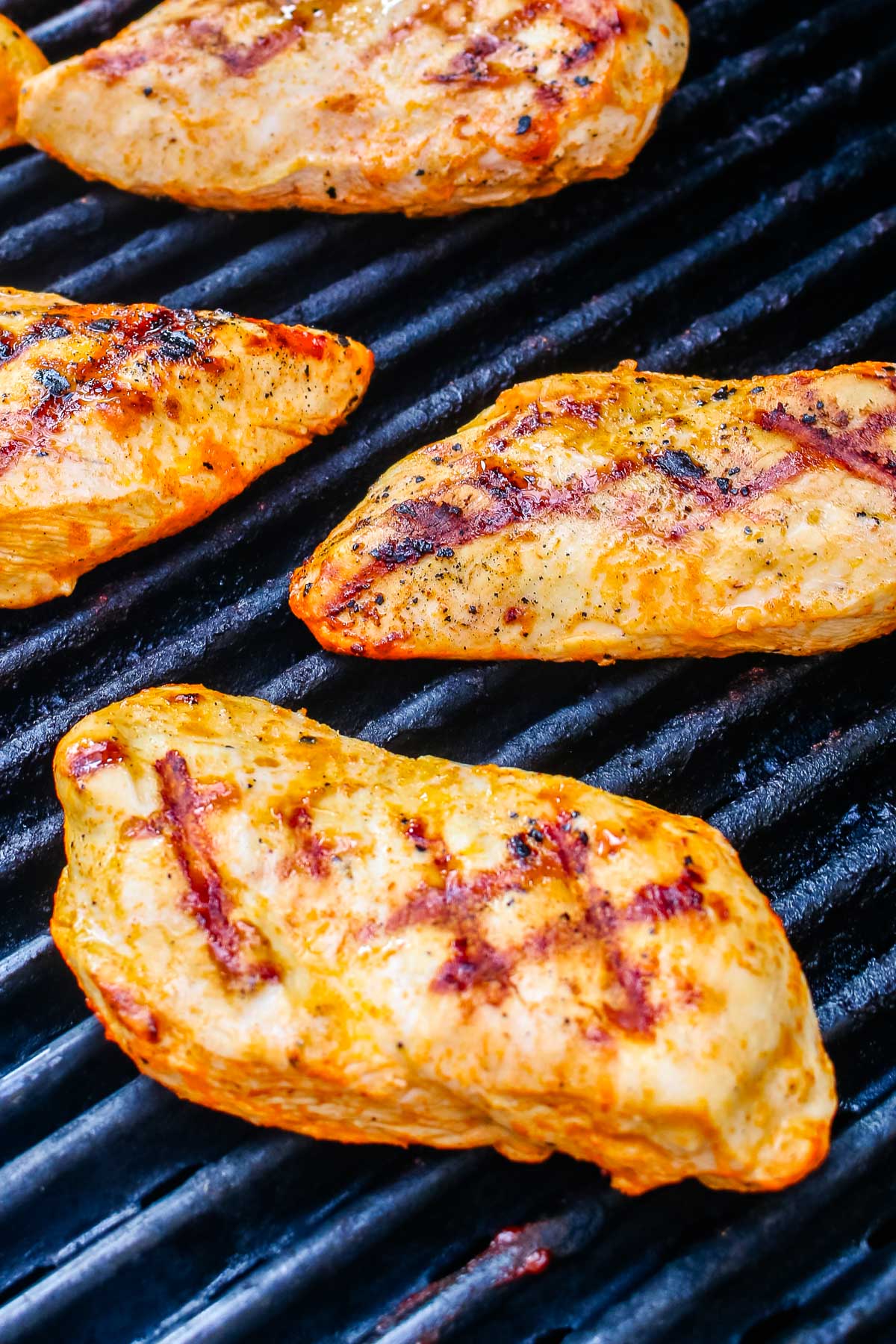 Buffalo chicken breasts cooking on outdoor grill grates with visible char marks.