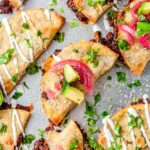 Overhead view of crispy black bean tacos on a baking sheet garnished with cilantro, avocado, pickled onions, and sour cream drizzle.