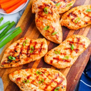 Grilled buffalo chicken breasts arranged on a wooden cutting board with green onions, carrots, celery, and ranch dressing.