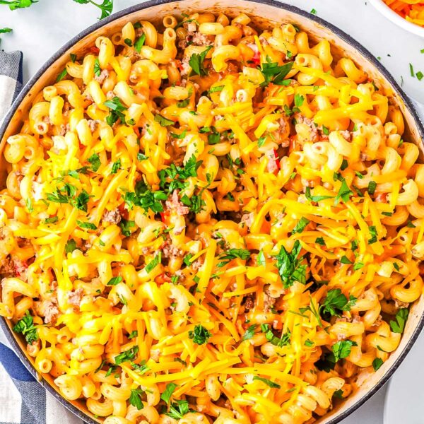 Overhead view of creamy Rotel pasta in a skillet topped with melted cheddar cheese and chopped parsley.