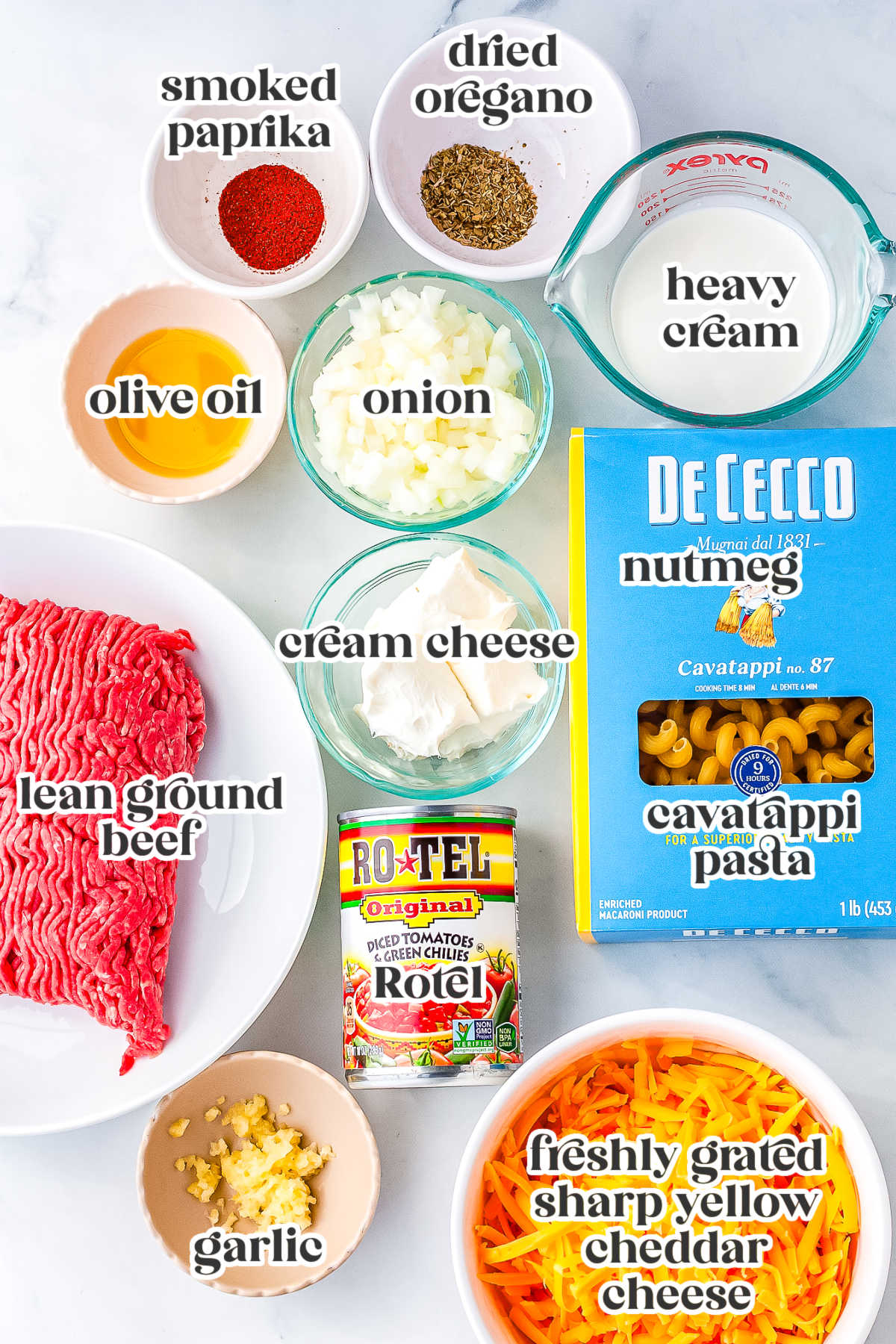 Ingredients for creamy Rotel pasta including ground beef, cavatappi pasta, cream cheese, cheddar, Rotel tomatoes, onion, garlic, and spices.