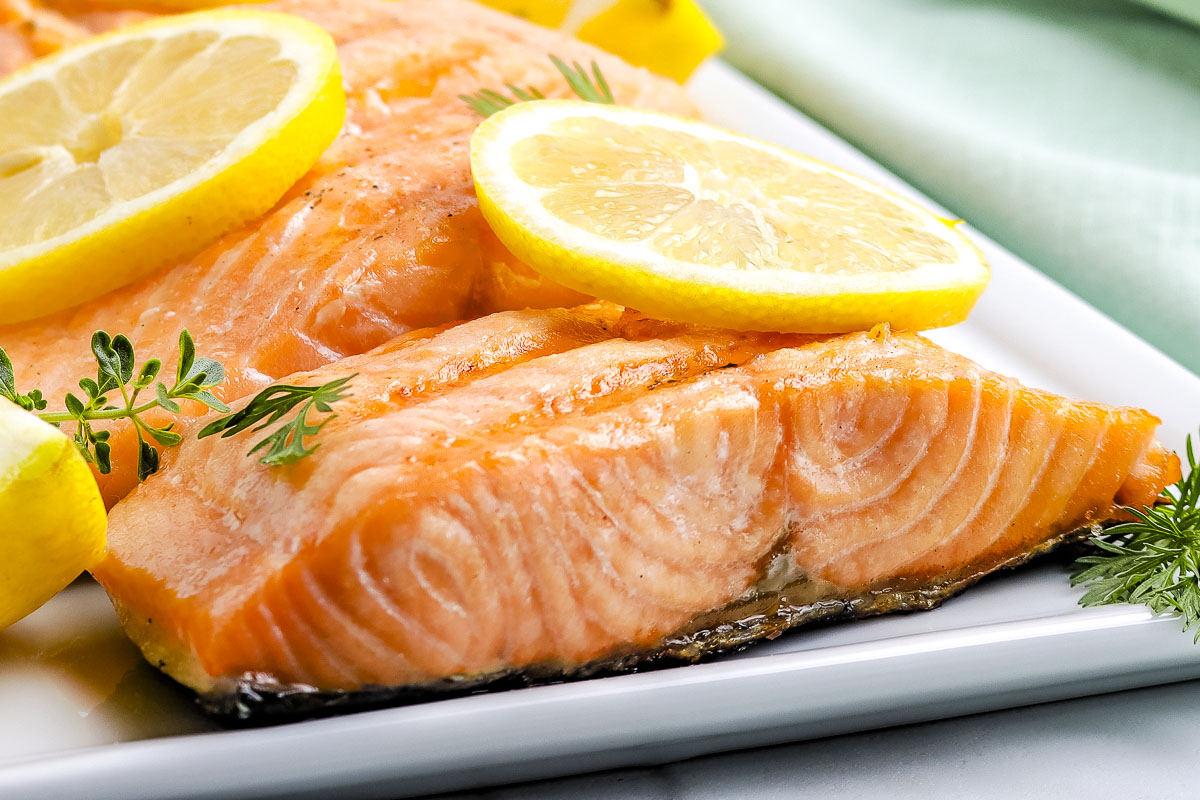 Close-up of grilled salmon topped with lemon slices and fresh herb garnish on a serving platter.
