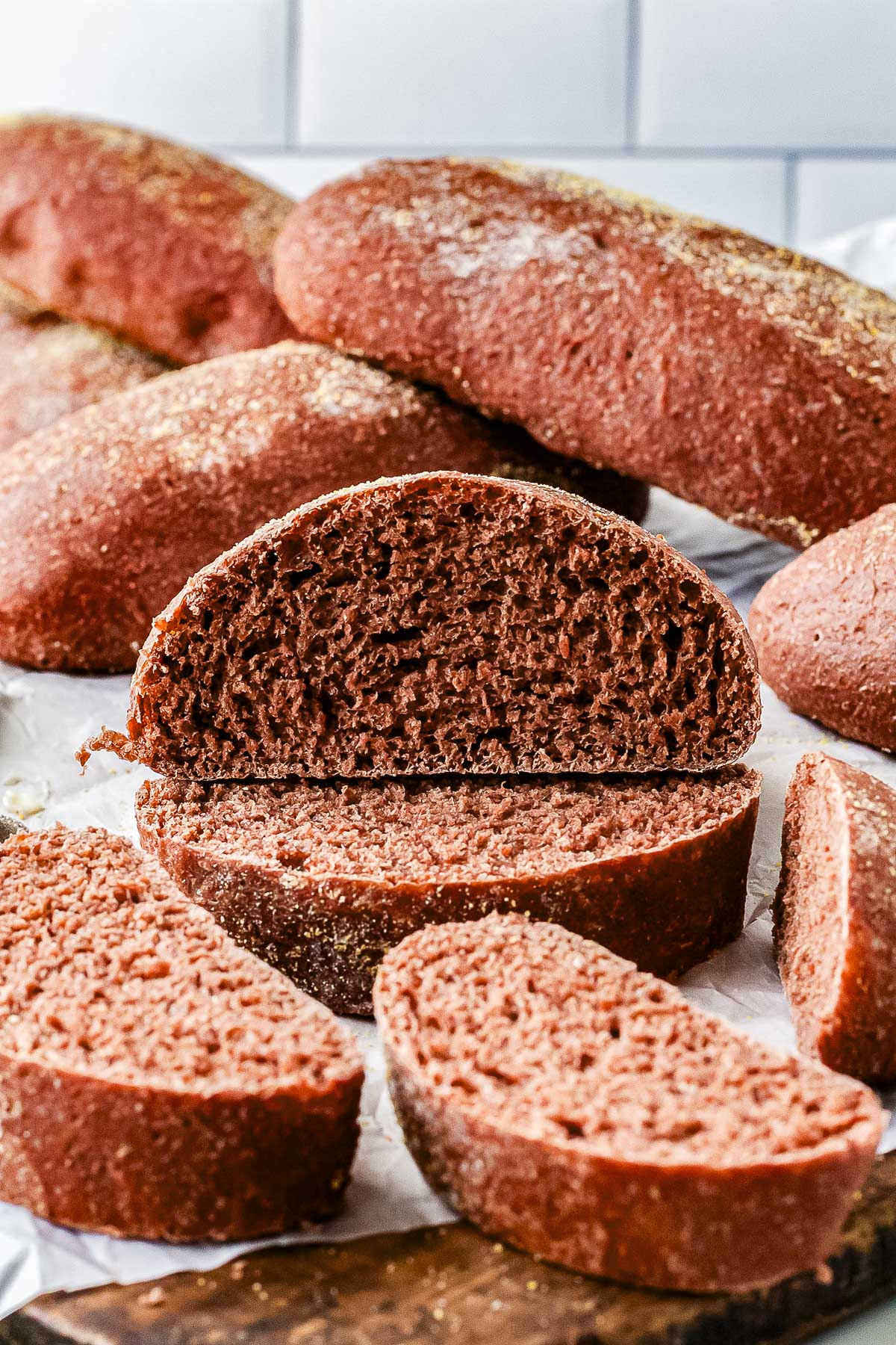 Sliced homemade Outback bread surrounded by baked loaves on parchment paper, showing the soft interior and dark brown crust dusted with cornmeal.
