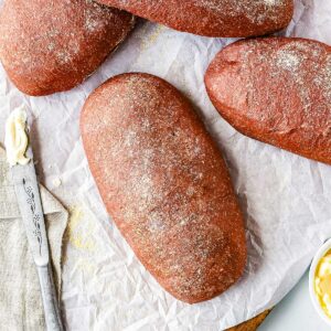 Overhead view of freshly baked homemade Outback bread loaves dusted with cornmeal on parchment paper beside butter and a bread knife.