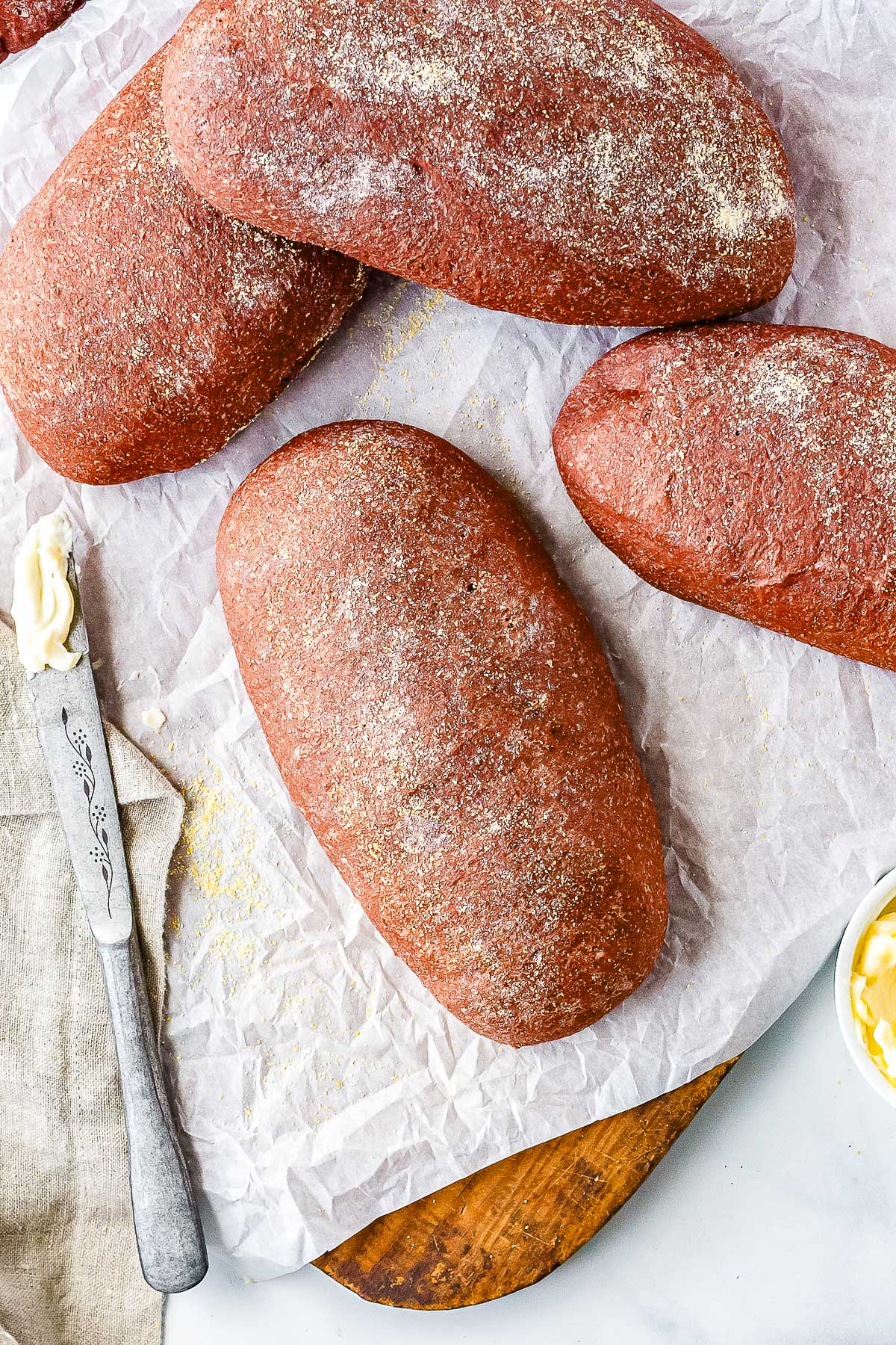Overhead view of freshly baked homemade Outback bread loaves dusted with cornmeal on parchment paper beside butter and a bread knife.