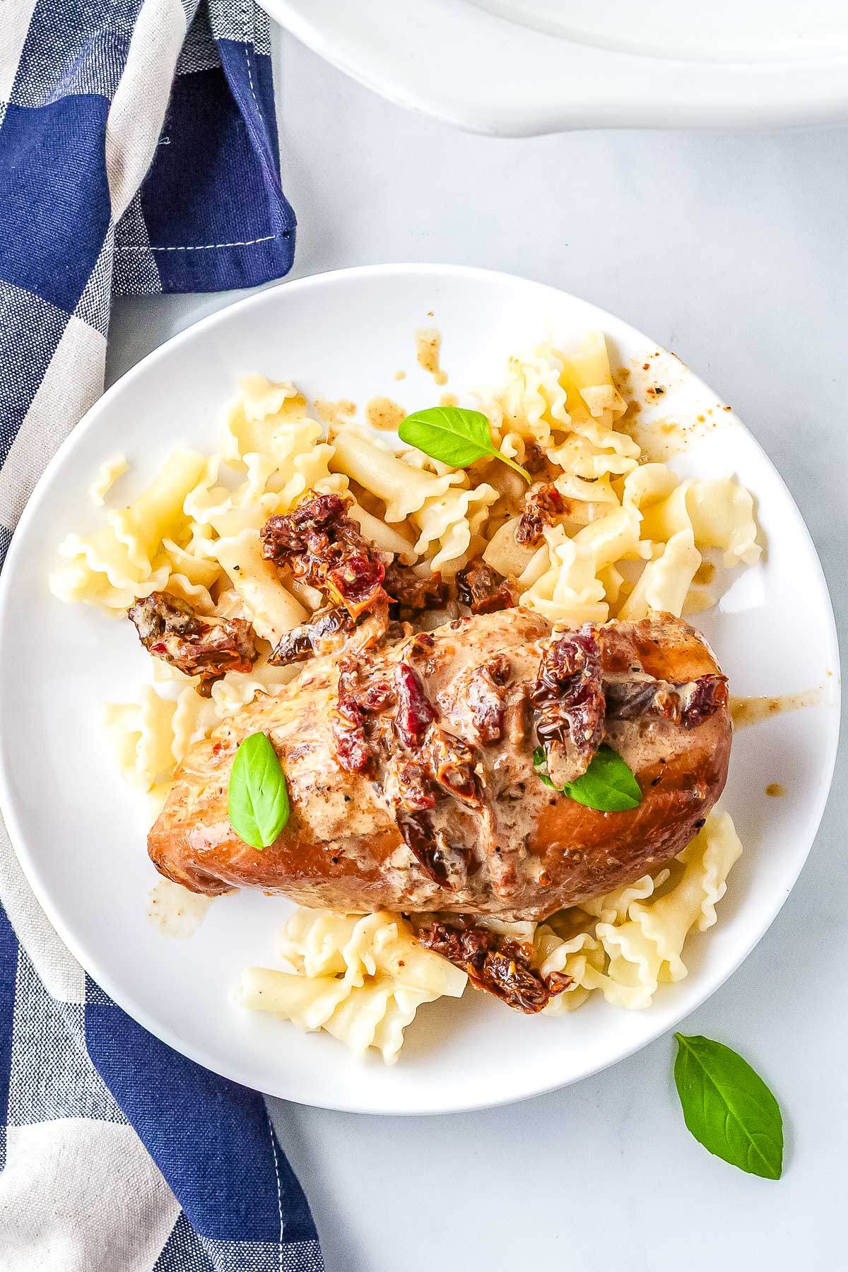 Crockpot Marry Me Chicken served over pasta with a creamy Parmesan sauce, sun-dried tomatoes, and fresh basil.