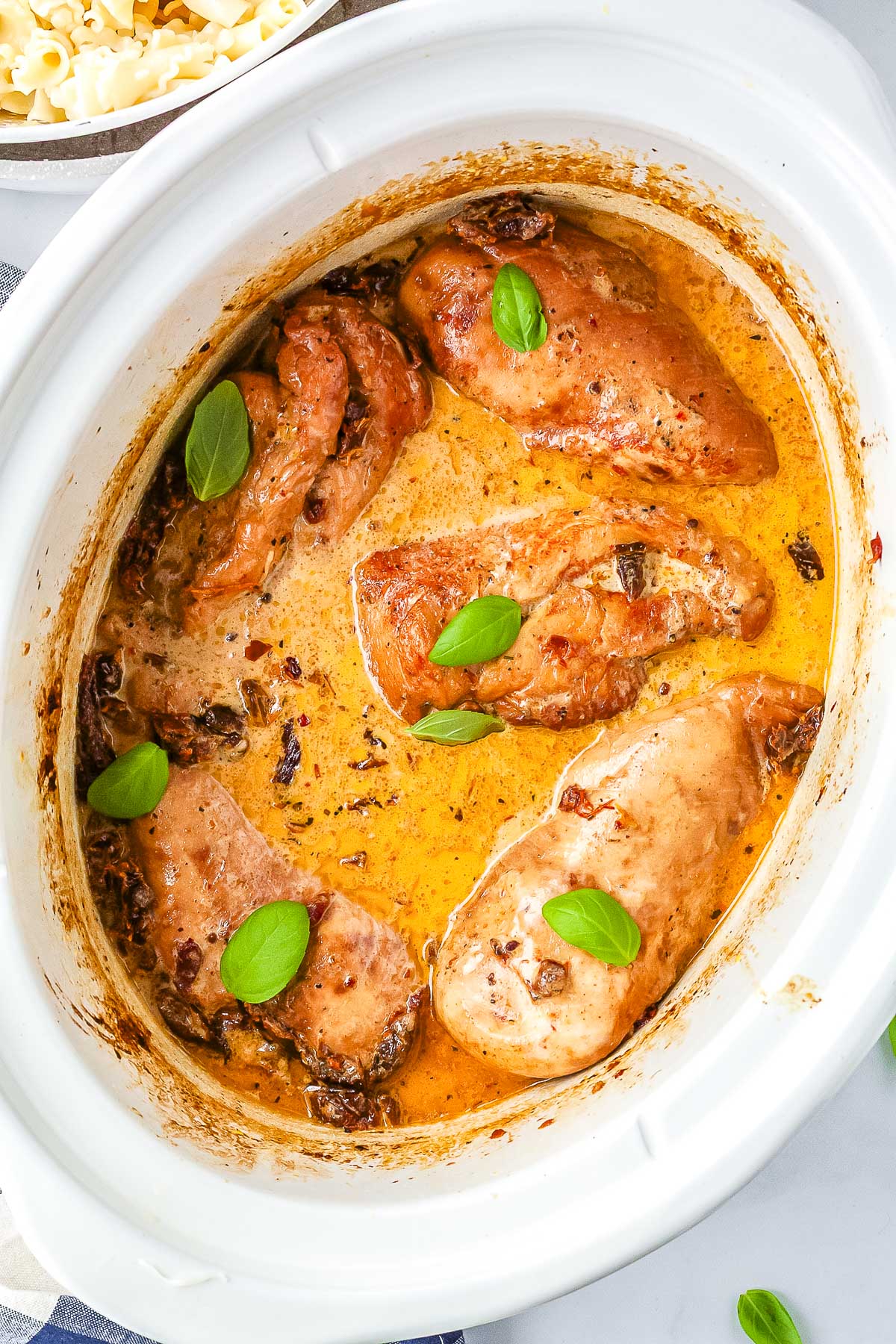 Creamy Crockpot Marry Me Chicken cooking in a slow cooker with Parmesan sauce, sun-dried tomatoes, and fresh basil garnish.