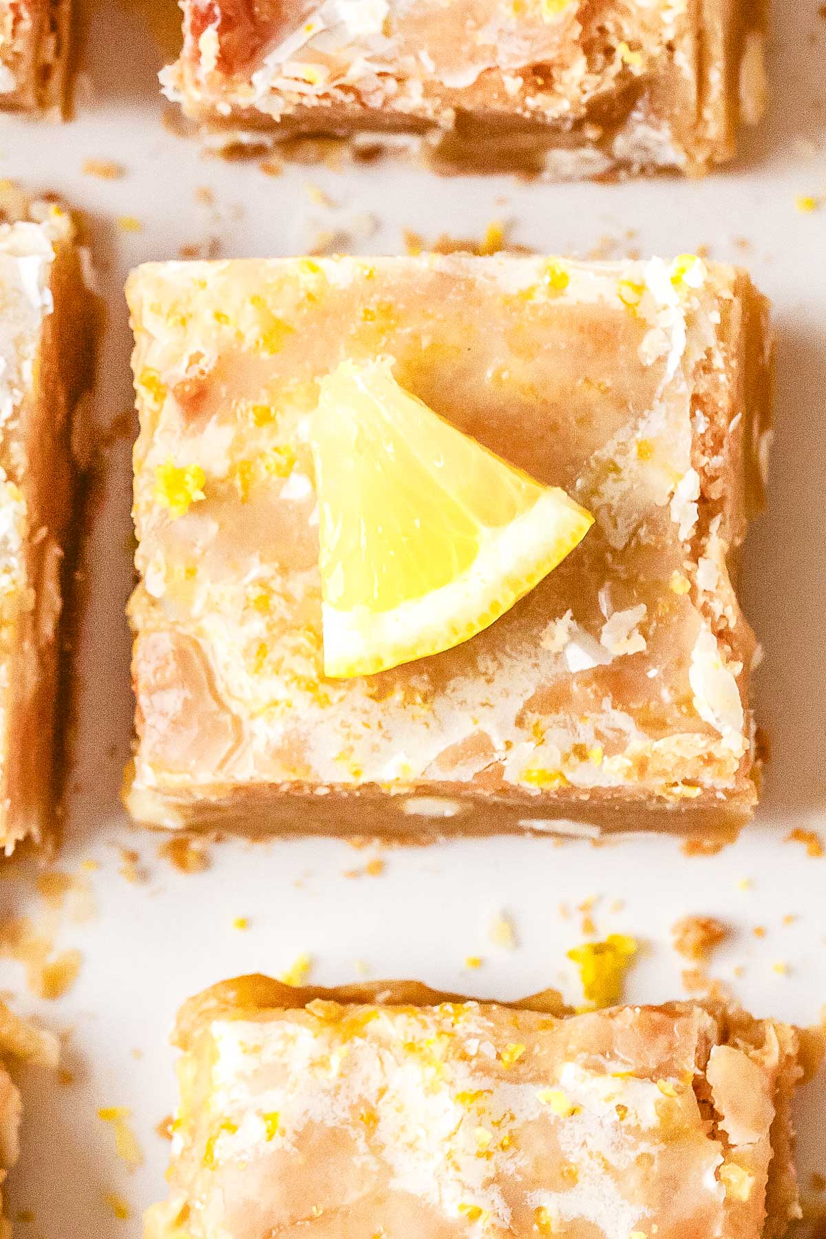 A close-up overhead view of a single square lemon blondie topped with a shiny glaze and a small fresh lemon wedge.