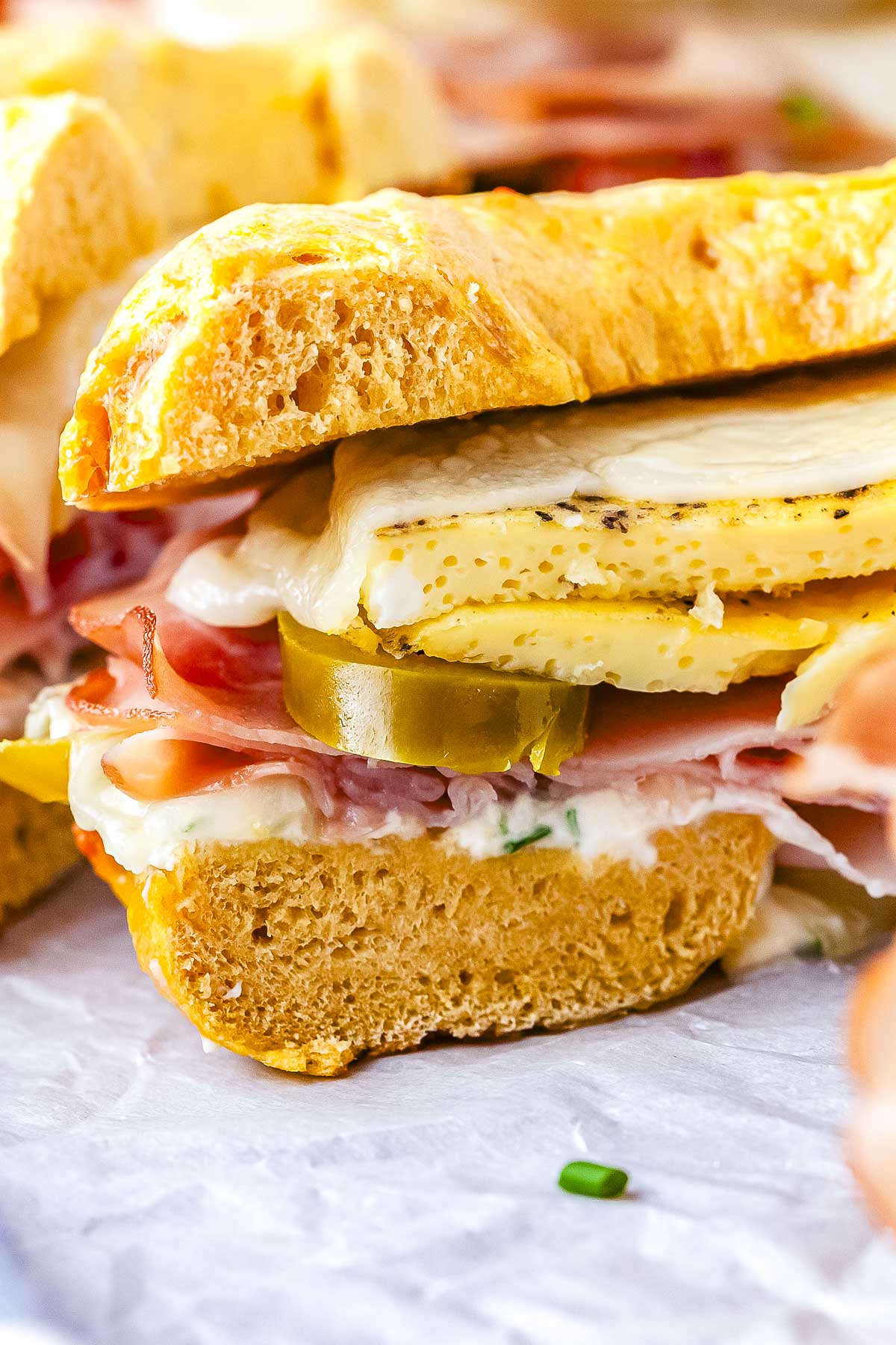 A close-up view of a sliced breakfast bagel sandwich showing layers of a baked egg round, honey ham, jalapeños, cream cheese spread, and melted cheese on an egg bagel.
