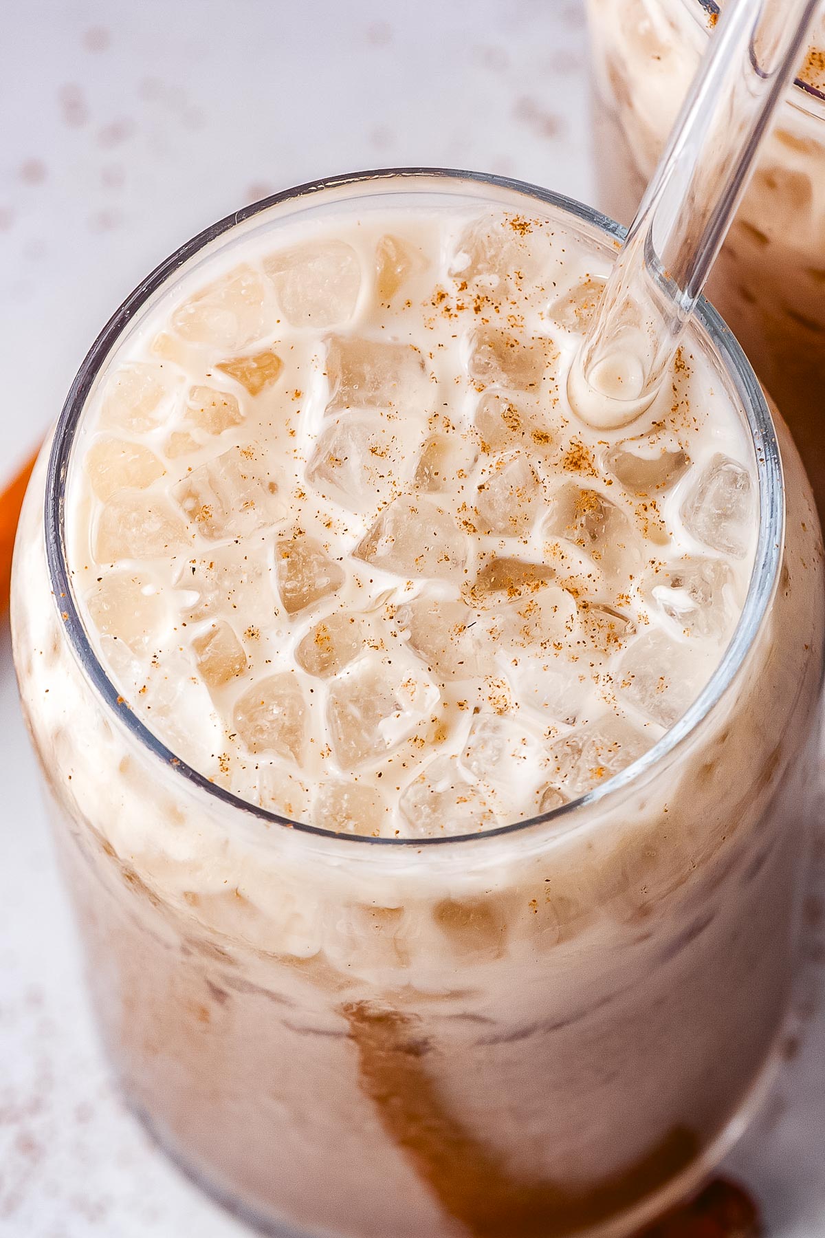 An overhead close-up view of a glass filled with crushed pebble ice, spiced dirty Dr Pepper, a splash of half-and-half, and a light dusting of ground cinnamon, served with a glass straw.