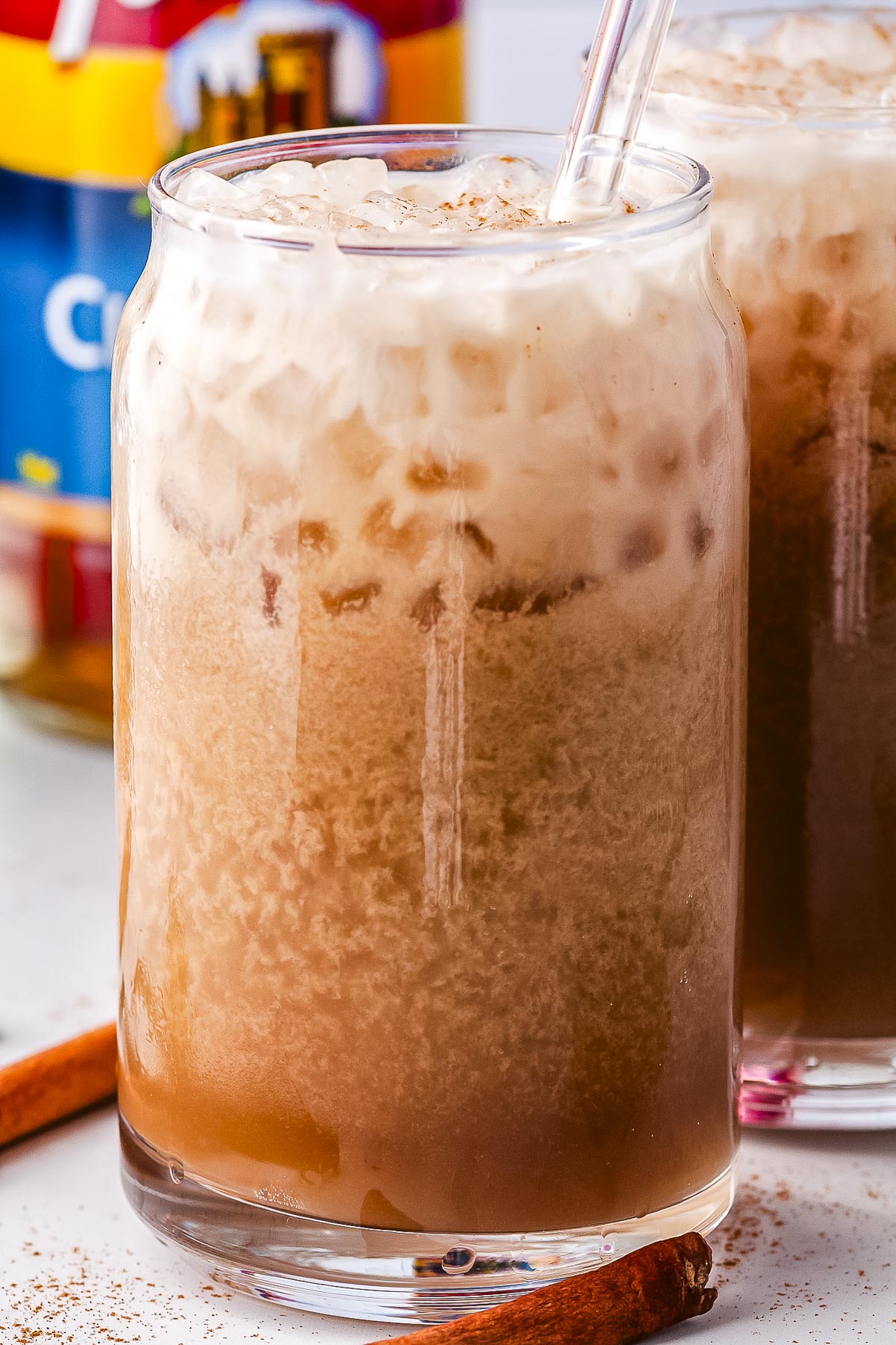 A can-shaped glass filled with iced dirty Dr Pepper mixed with spiced syrups and sweet half-and-half, topped with ground cinnamon and served with a clear straw.