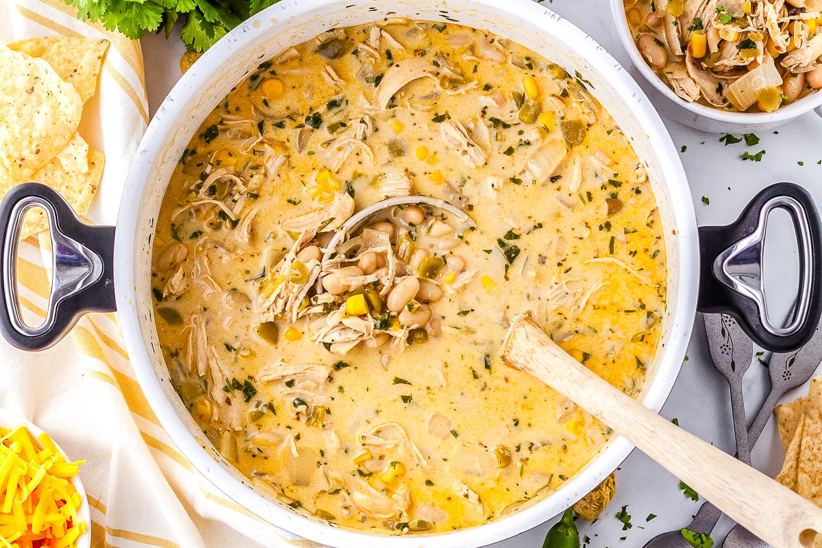 Overhead view of a large pot of creamy white chicken chili filled with shredded chicken, white beans, corn, and green chiles, with a ladle resting in the center.