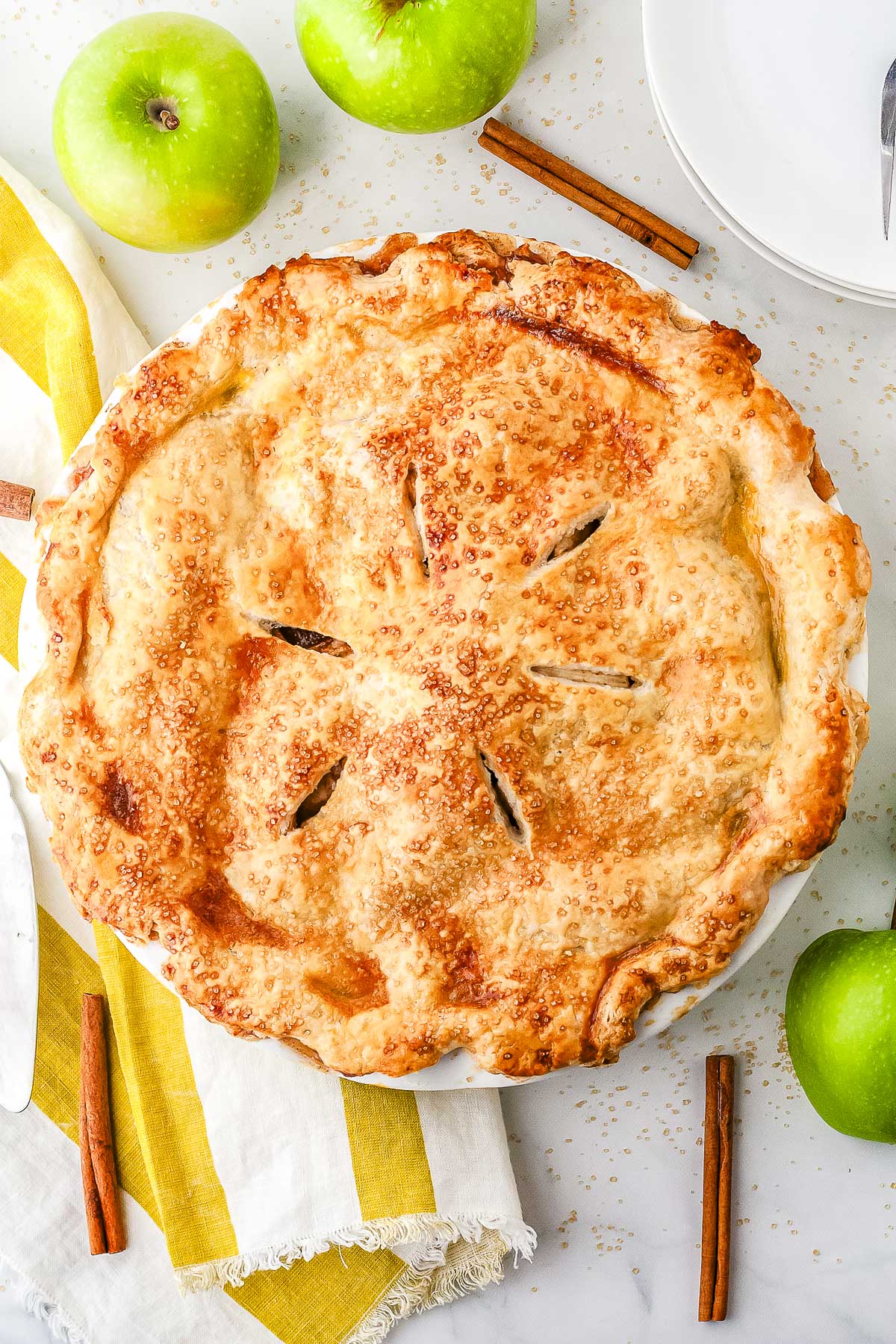 An overhead view of a golden brown salted caramel apple pie with a crimped butter crust and decorative steam vents sprinkled with turbinado sugar.
